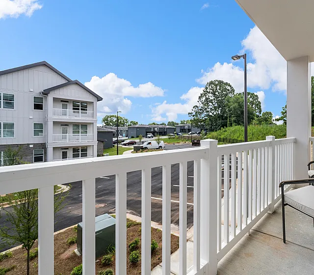 Inviting apartment balcony with seating offering a scenic view of lush greenery and modern buildings under a clear blue sky.