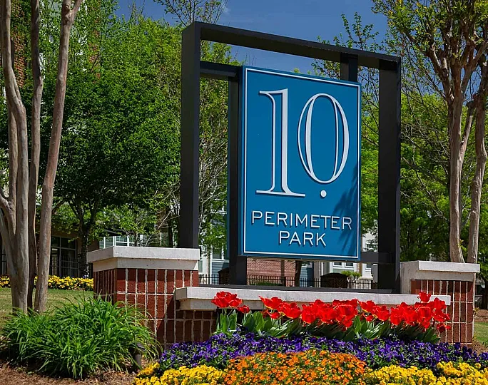 Inviting entrance sign of 10 Perimeter Park surrounded by vibrant flowers and lush greenery, showcasing a welcoming community.