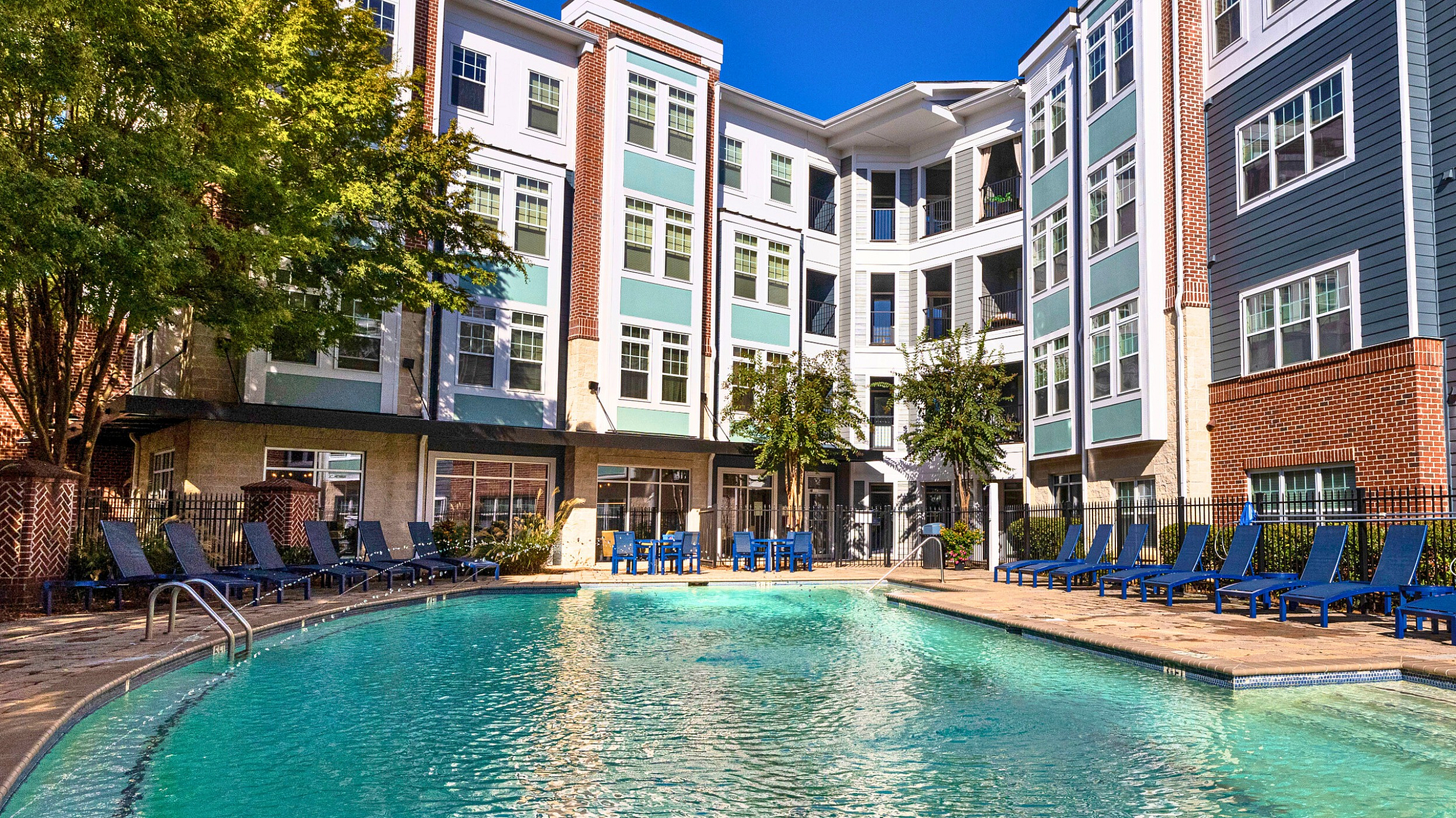 Luxurious apartment complex featuring a sparkling pool surrounded by comfortable lounge chairs and vibrant greenery.