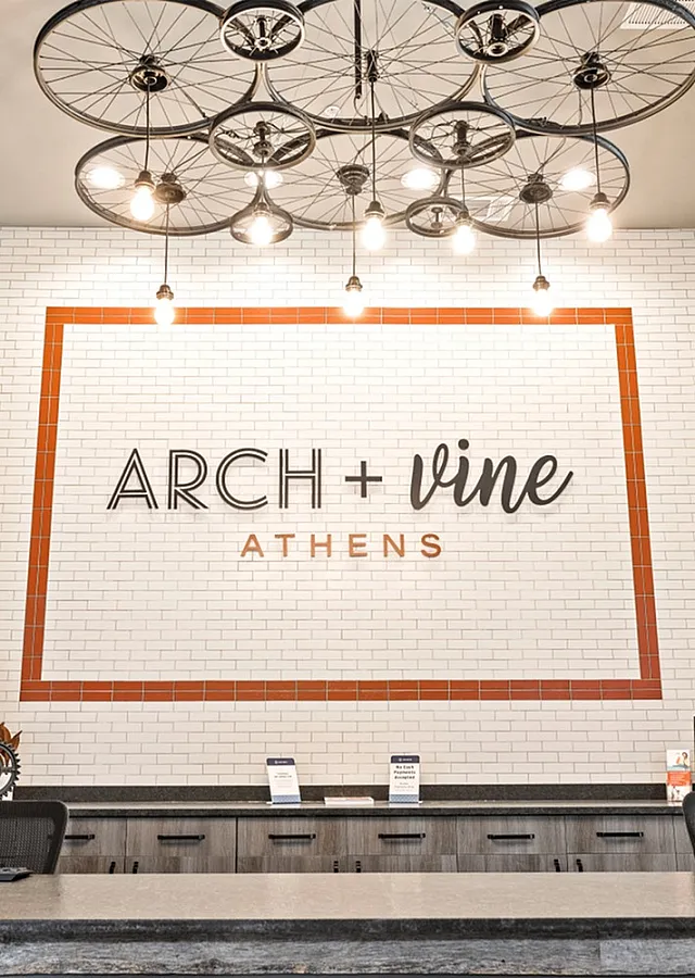 Chic lobby area featuring a modern front desk with branded wall art at Arch + Vine in Athens, highlighted by unique bicycle wheel ceiling lights.