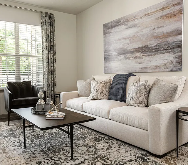 Inviting living room with plush beige sofa, elegant artwork, and natural light streaming through large windows.