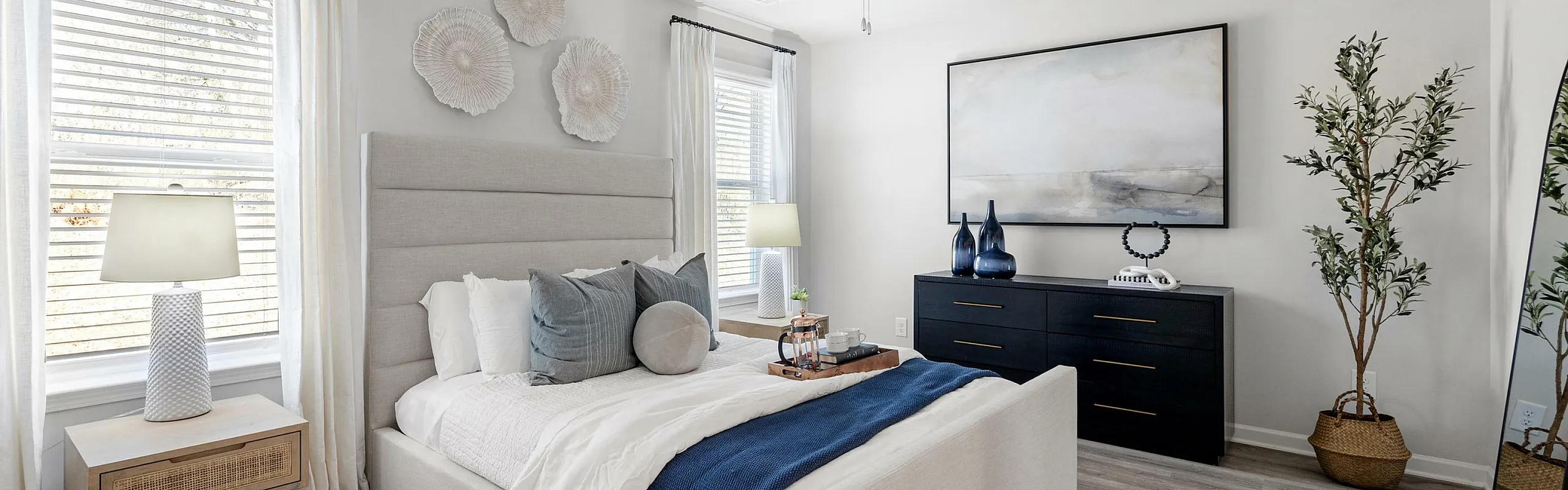 Bright and inviting bedroom with elegant decor, featuring a cozy bed, stylish dresser, and large windows with natural light.