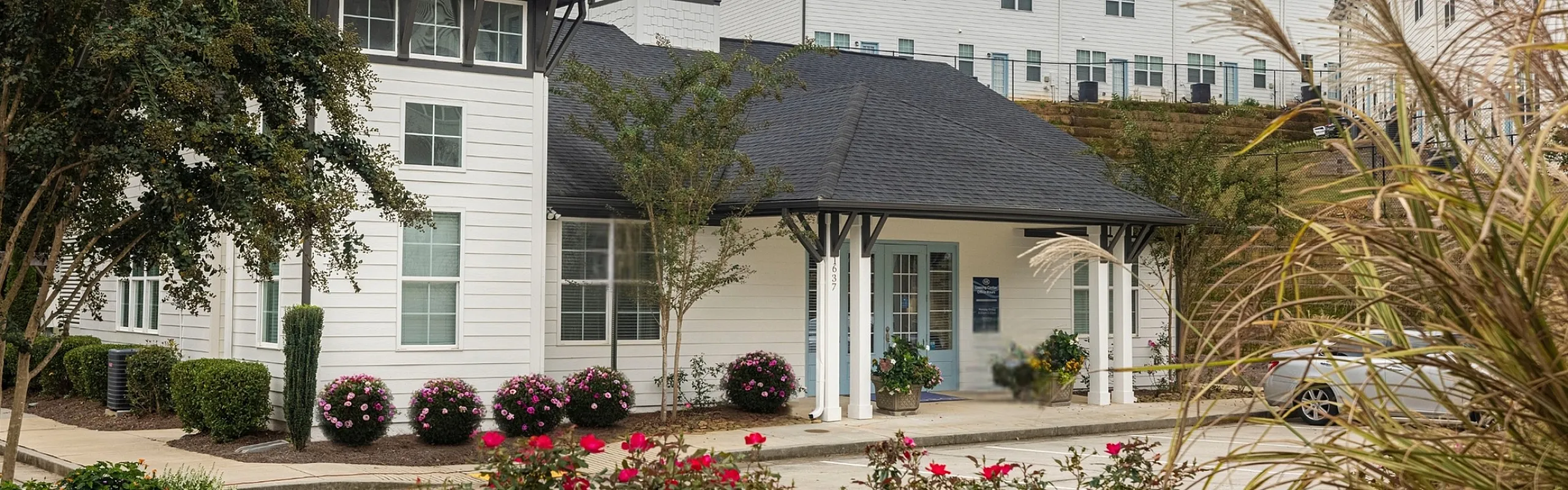 Charming residential community with modern white buildings, lush landscaping, and vibrant flowers, offering serene living.