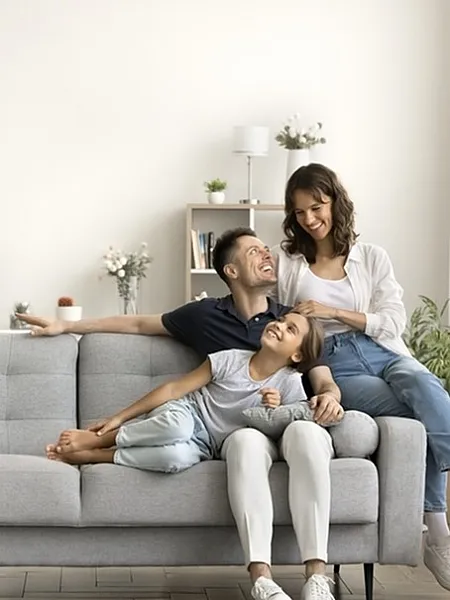 Bright, inviting living room with a cozy gray sofa, abundant natural light, and a warm family atmosphere. Modern shelving and decor accents add a stylish touch.