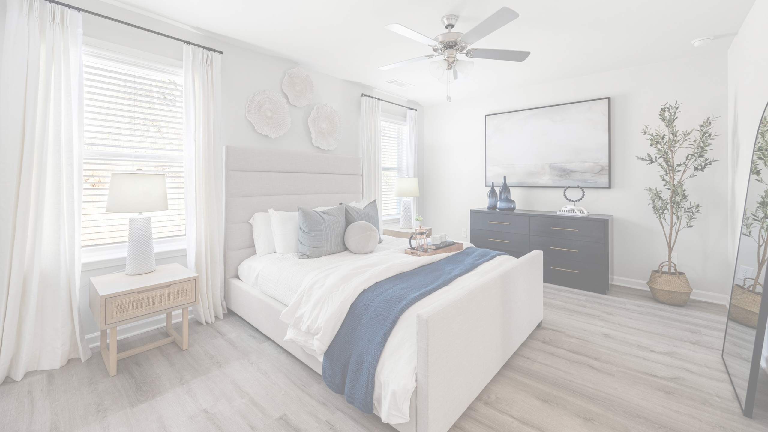 Bright and elegant bedroom with plush bedding, stylish decor, a sleek dresser, and natural light streaming through large windows.