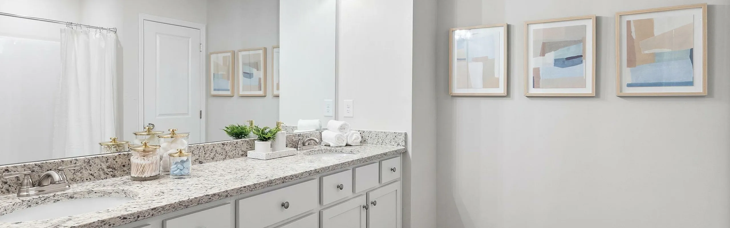 Elegant bathroom featuring a granite double vanity, modern lighting fixtures, and stylish framed artwork on the walls.