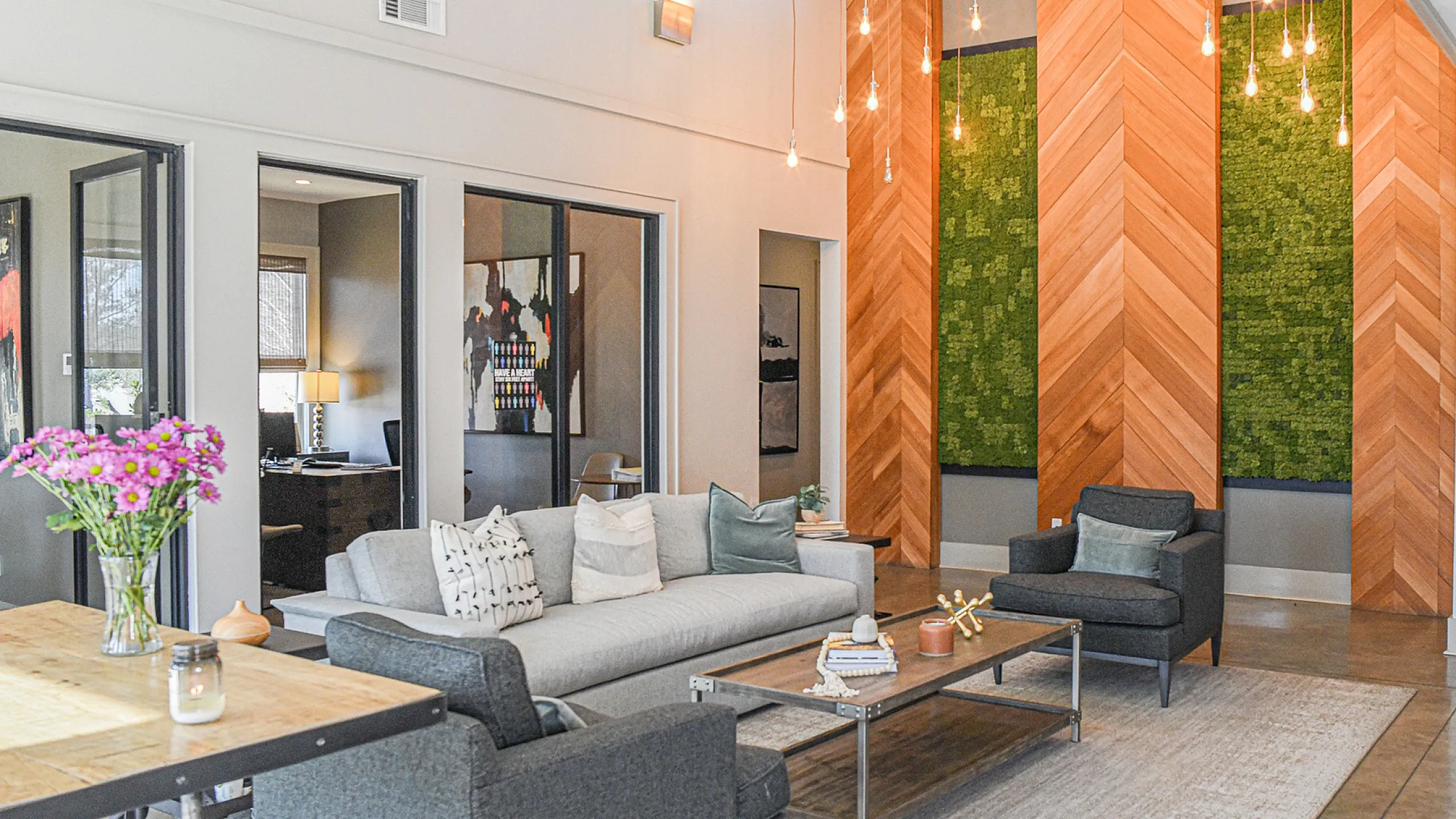 Contemporary living room with high ceilings, stylish lighting, and modern decor. Features sleek gray furniture, vibrant artwork, and a cozy atmosphere.