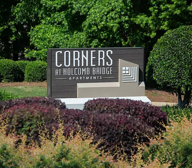 Charming entrance sign for Corners at Holcomb Bridge Apartments, surrounded by lush greenery and vibrant landscaping.