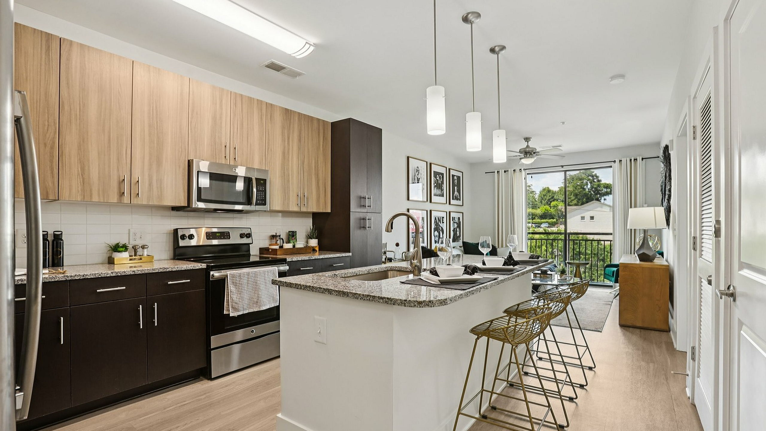 Modern open-concept apartment kitchen with sleek cabinetry, granite countertops, and stylish pendant lighting, leading to a bright living area with large windows and tasteful decor.