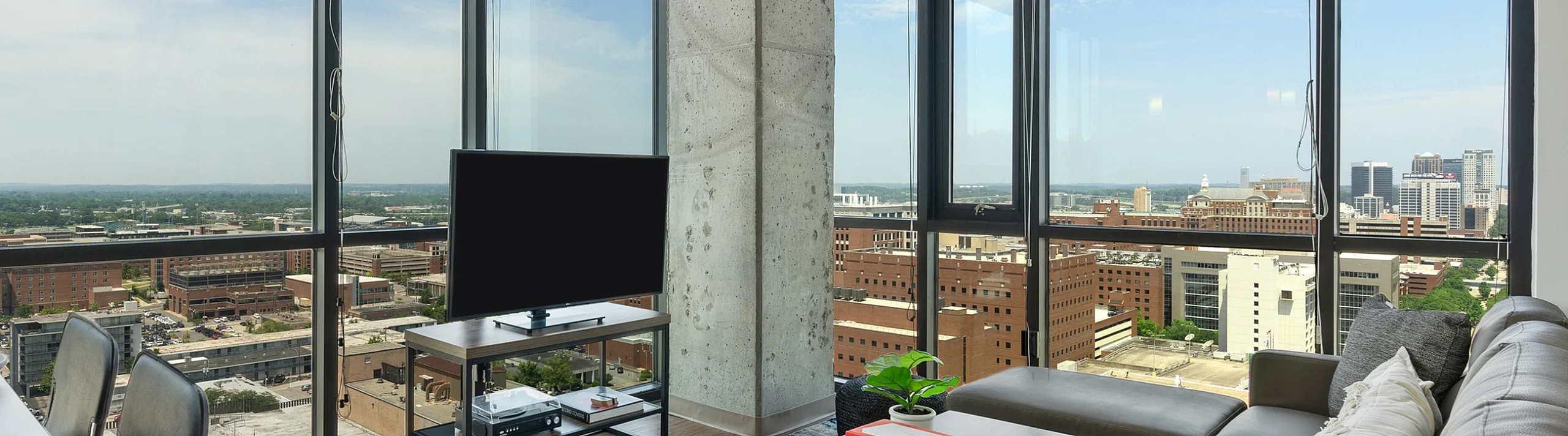 Modern apartment living room with floor-to-ceiling windows offering a stunning panoramic city view, featuring a cozy gray sofa, sleek decor, and abundant natural light.