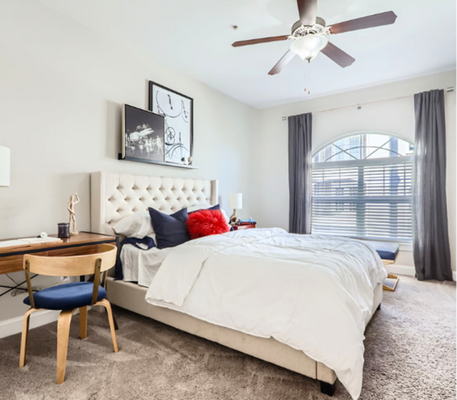 Bright and inviting bedroom featuring a plush king-sized bed with elegant tufted headboard, stylish wooden desk, and large arched window for natural light.