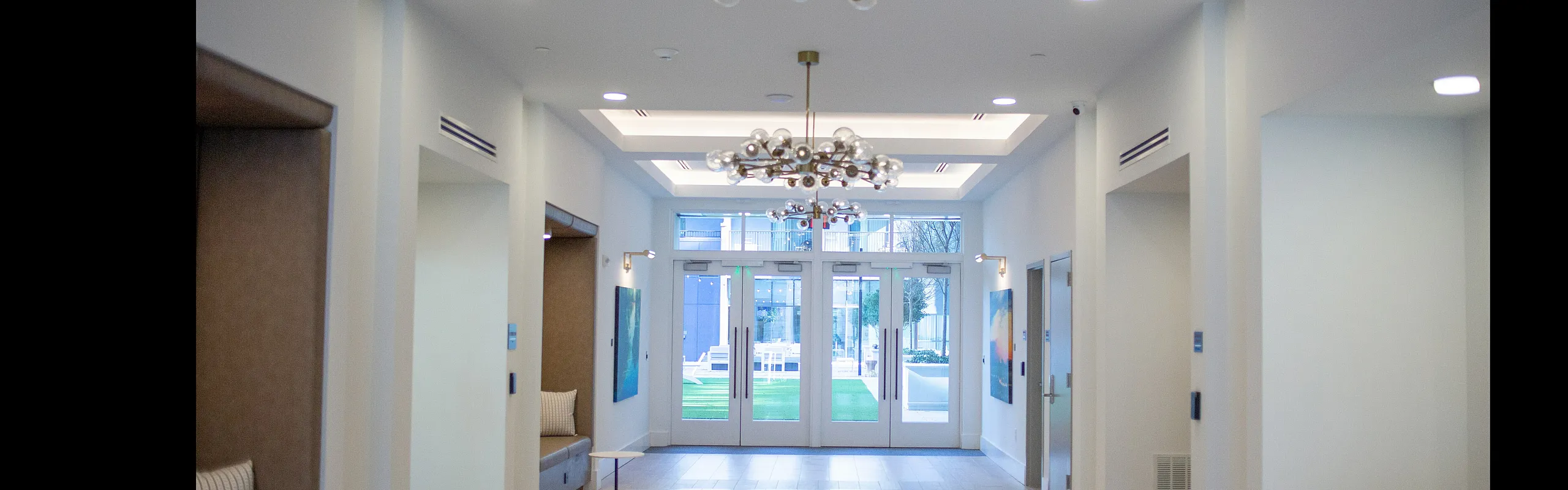 Bright and modern lobby with elegant chandeliers, sophisticated seating areas, and large glass doors opening to a vibrant outdoor space.