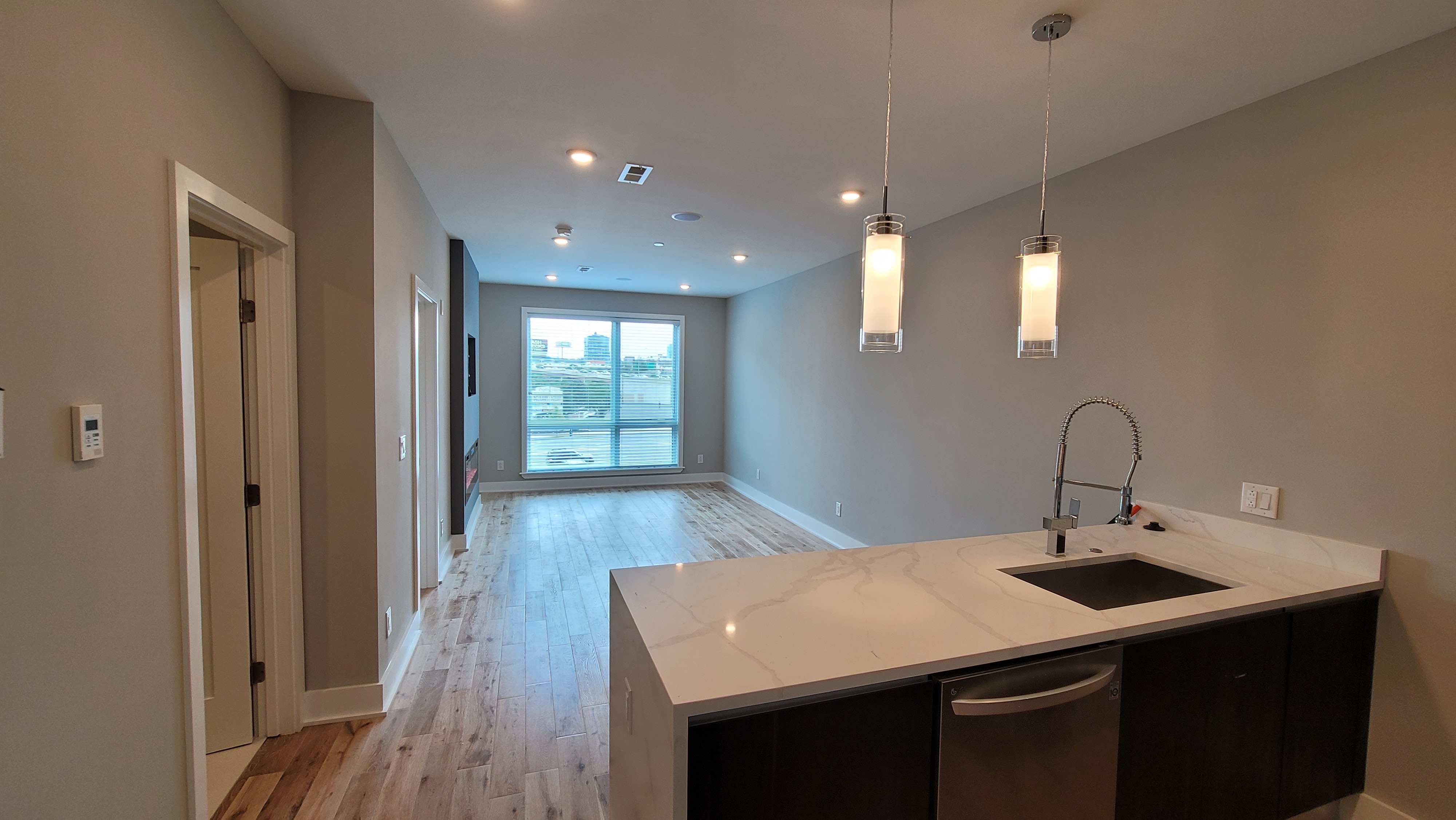 Modern apartment interior with open-concept kitchen featuring sleek countertops and elegant pendant lighting, leading to a bright living area with large windows and stylish hardwood floors.