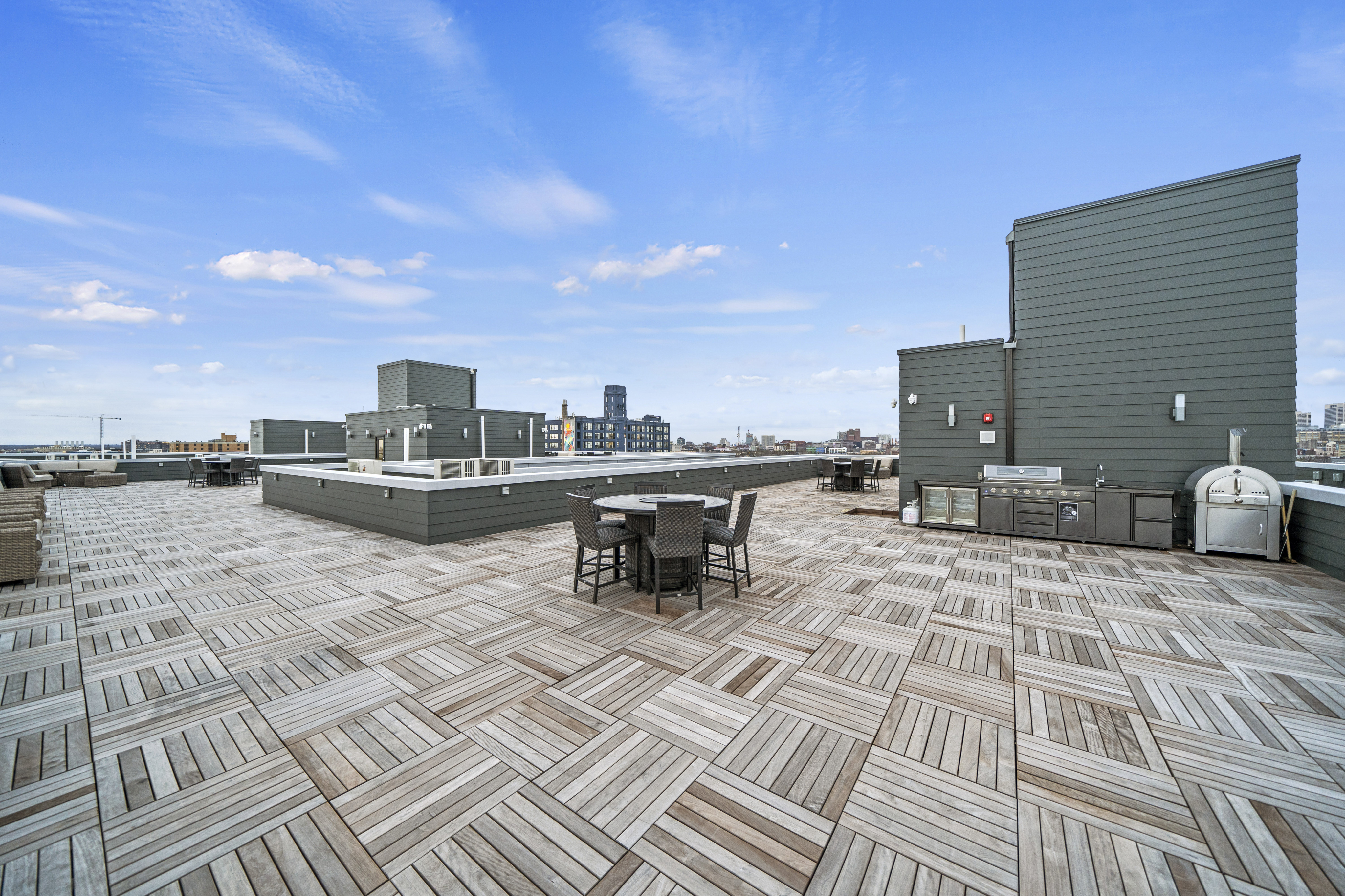 Expansive rooftop terrace with modern outdoor furniture and a built-in BBQ grill, offering stunning skyline views under a clear blue sky.