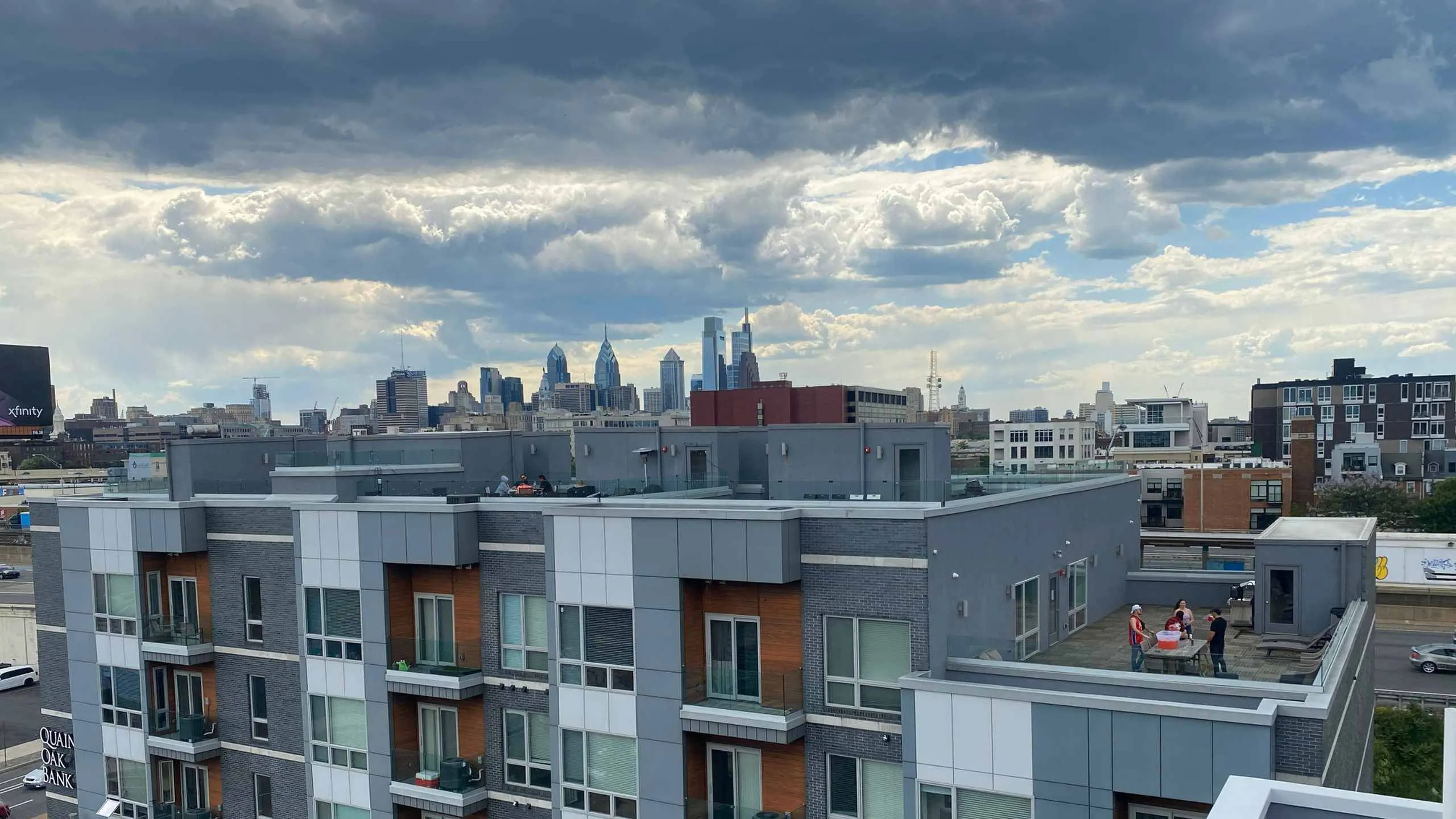Modern apartment building with private rooftop terrace offering stunning city skyline views under dramatic skies.