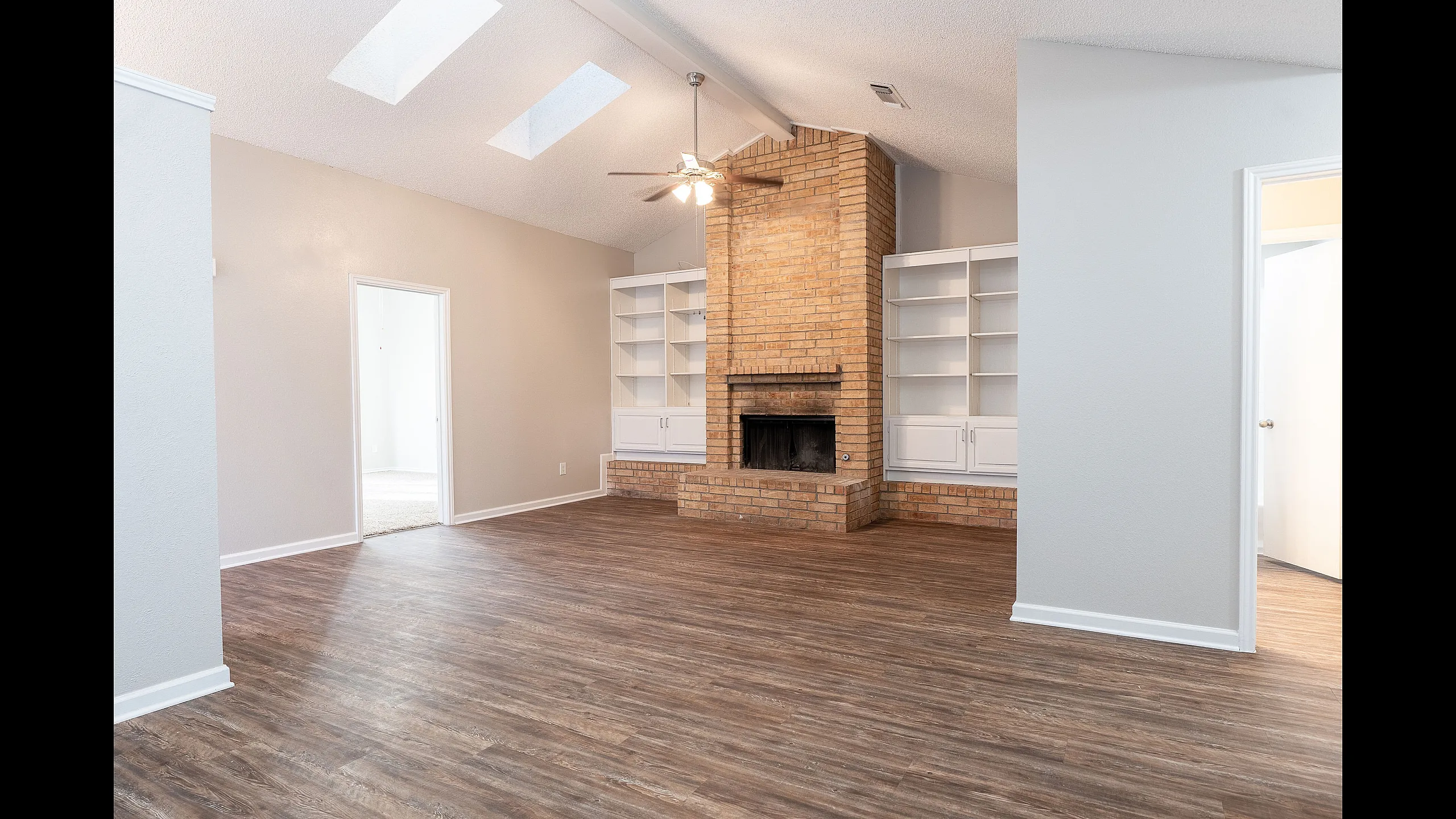 Bright and inviting living room with rustic brick fireplace, elegant built-in bookshelves, and sleek wooden flooring, enhanced by natural light from skylights.