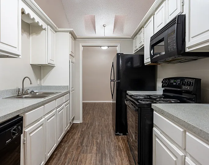 Modern apartment kitchen with sleek black appliances, white cabinetry, and wood-style flooring, creating a clean and inviting culinary space.