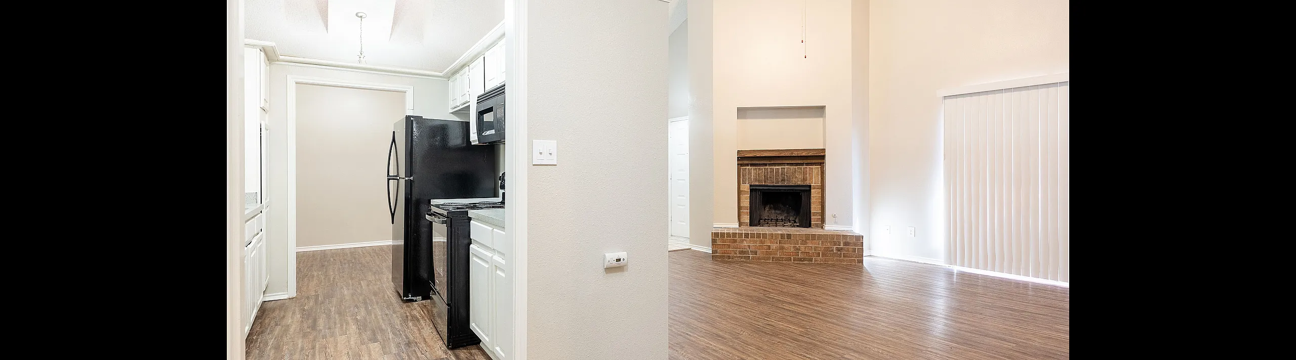 Modern apartment interior showcasing an inviting open-concept living space with a cozy brick fireplace, sleek kitchen with white cabinetry, and elegant wood flooring throughout.
