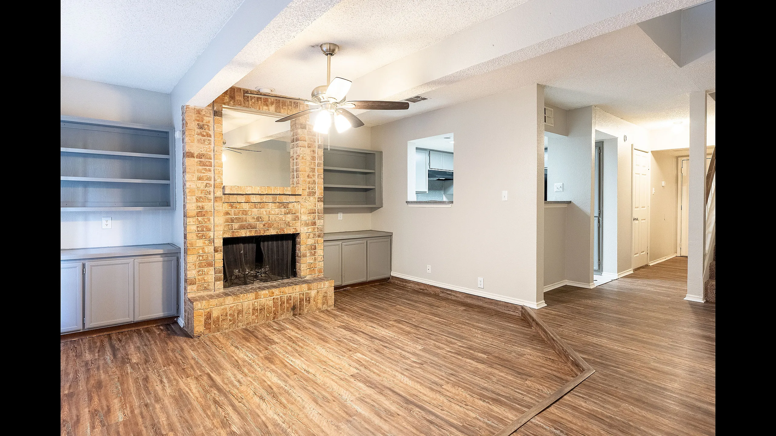 Inviting living area with elegant wood flooring, a charming brick fireplace, and built-in shelving, perfect for cozy gatherings.