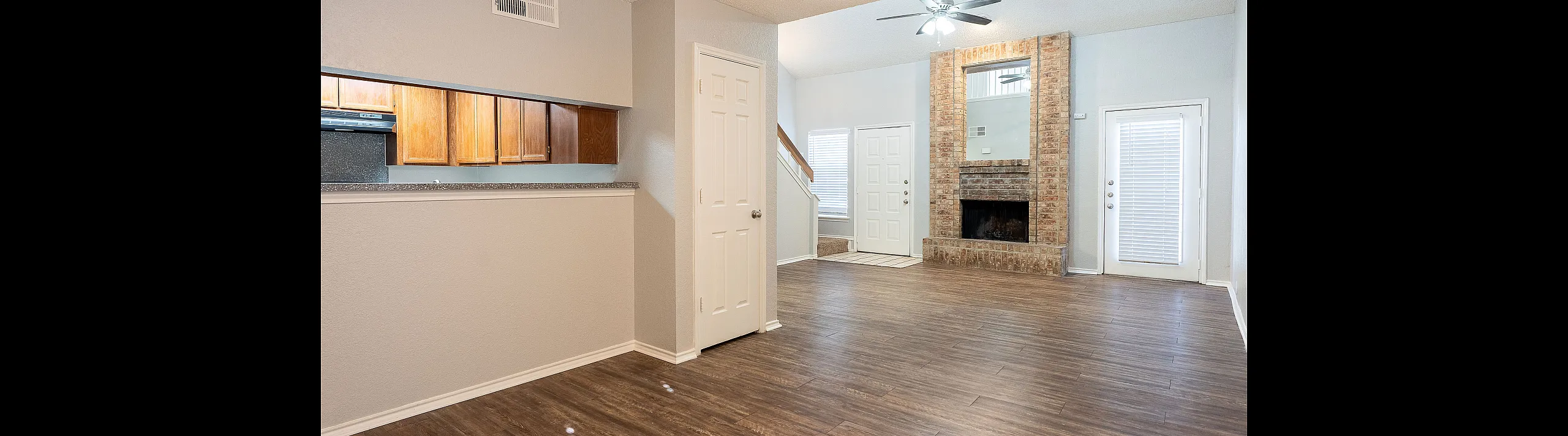 Bright, open-concept living area with elegant wood flooring, charming brick fireplace, and modern kitchen with ample cabinetry.