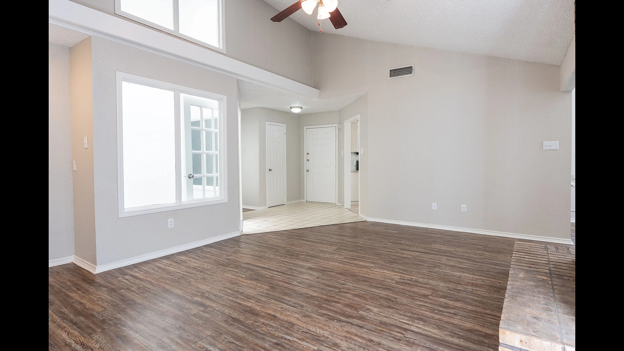 Bright and airy living space with elegant hardwood flooring, vaulted ceiling, and large window for natural light.
