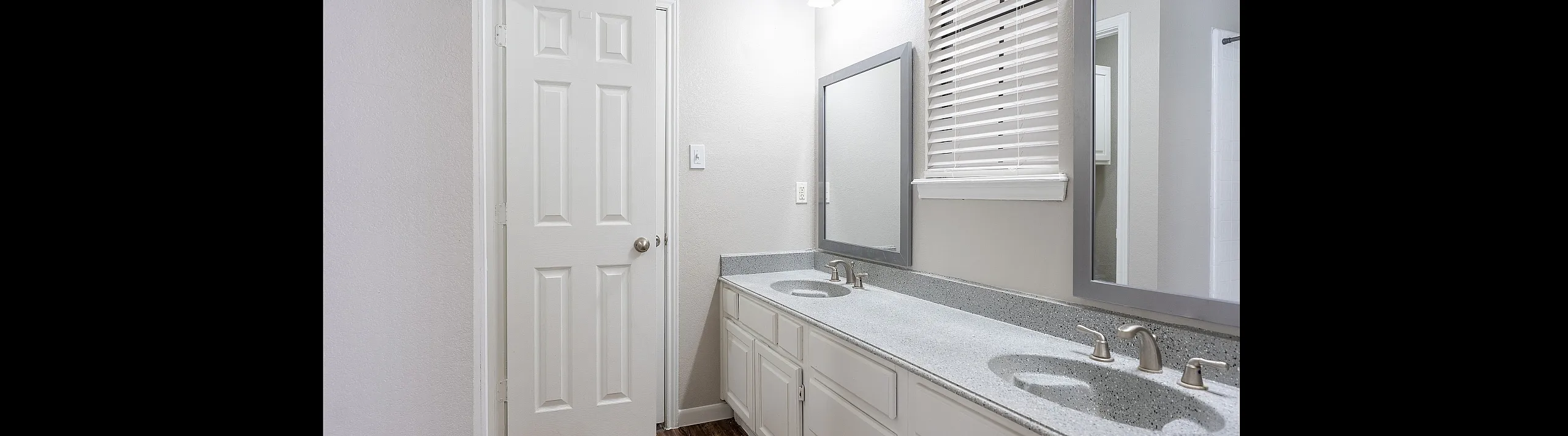 Modern bathroom featuring dual sinks, elegant countertop, large mirrors, and natural light from window blinds.