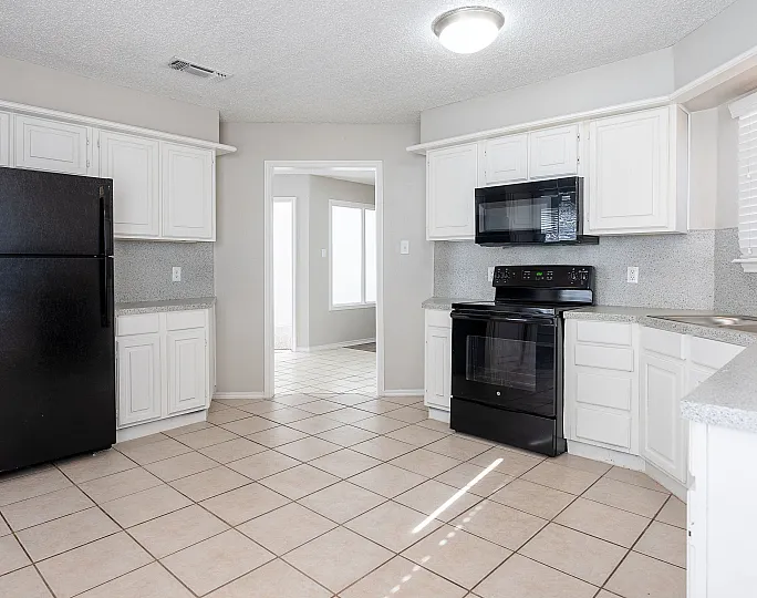 Bright and inviting kitchen featuring sleek black appliances, ample white cabinetry, and modern countertops with a view into the spacious dining area.