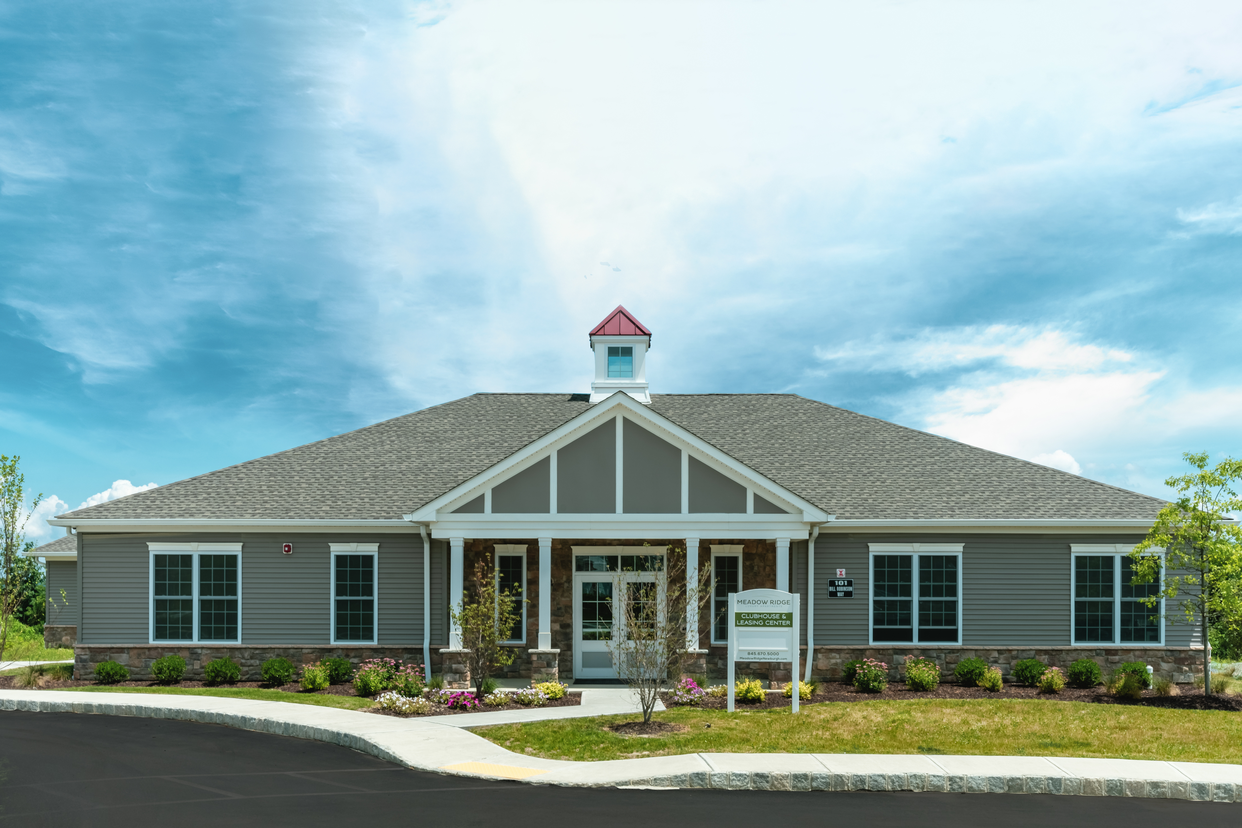 Charming clubhouse with modern gray siding and a welcoming front entrance surrounded by lush landscaping.