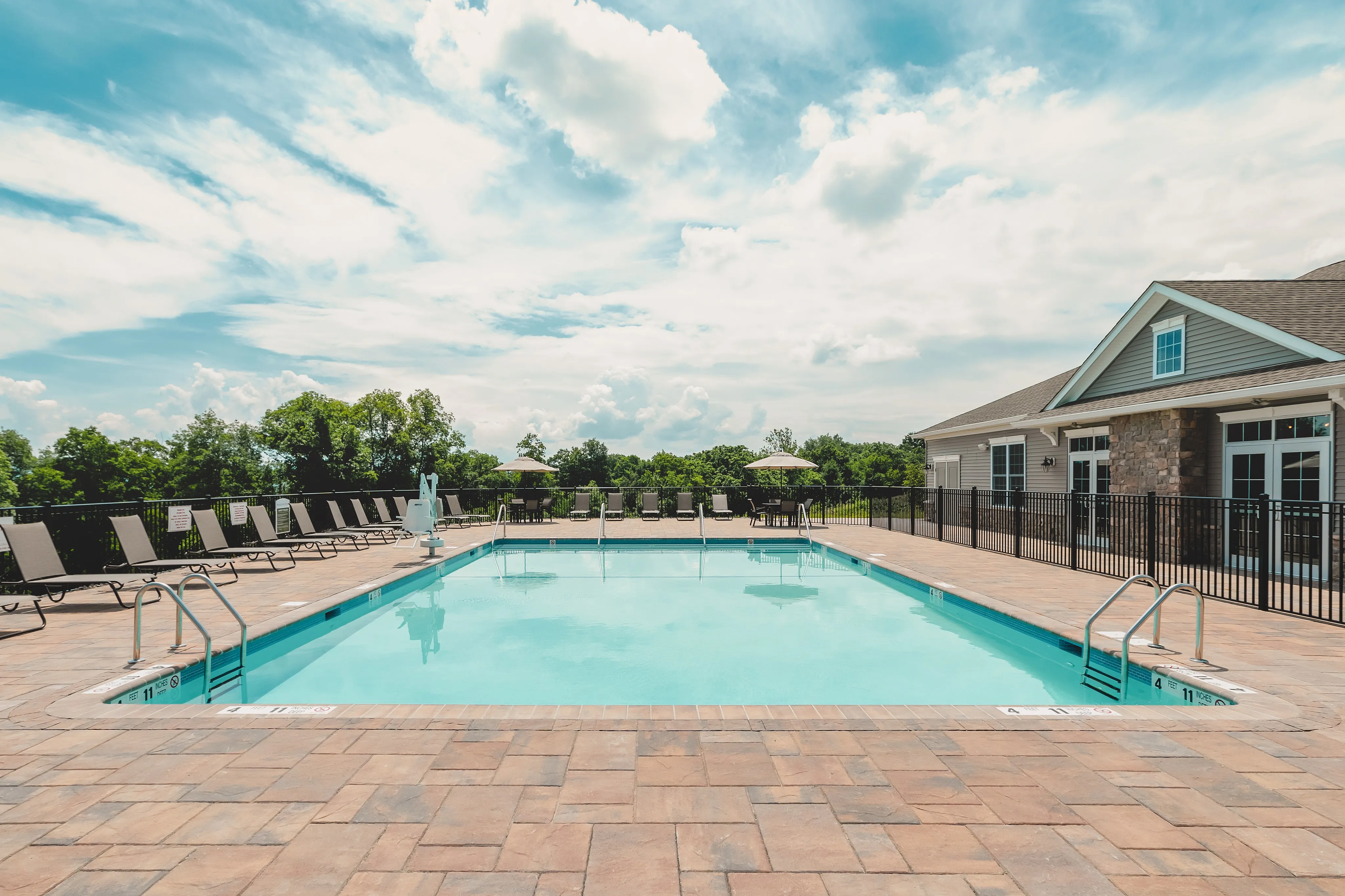 Inviting swimming pool with lounge chairs under a bright blue sky, surrounded by lush greenery.