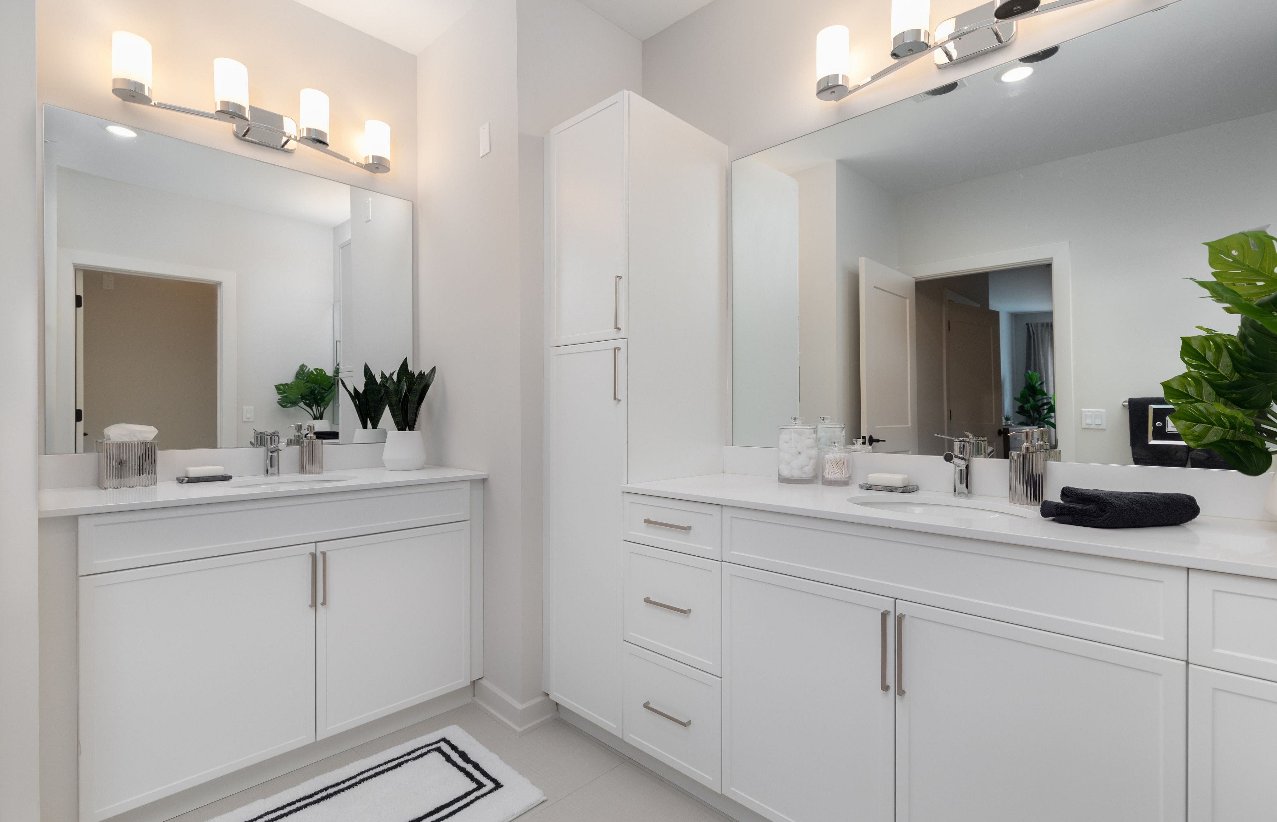 Luxurious and spacious bathroom with bright vanity lights, dual sinks, and sleek white cabinetry.