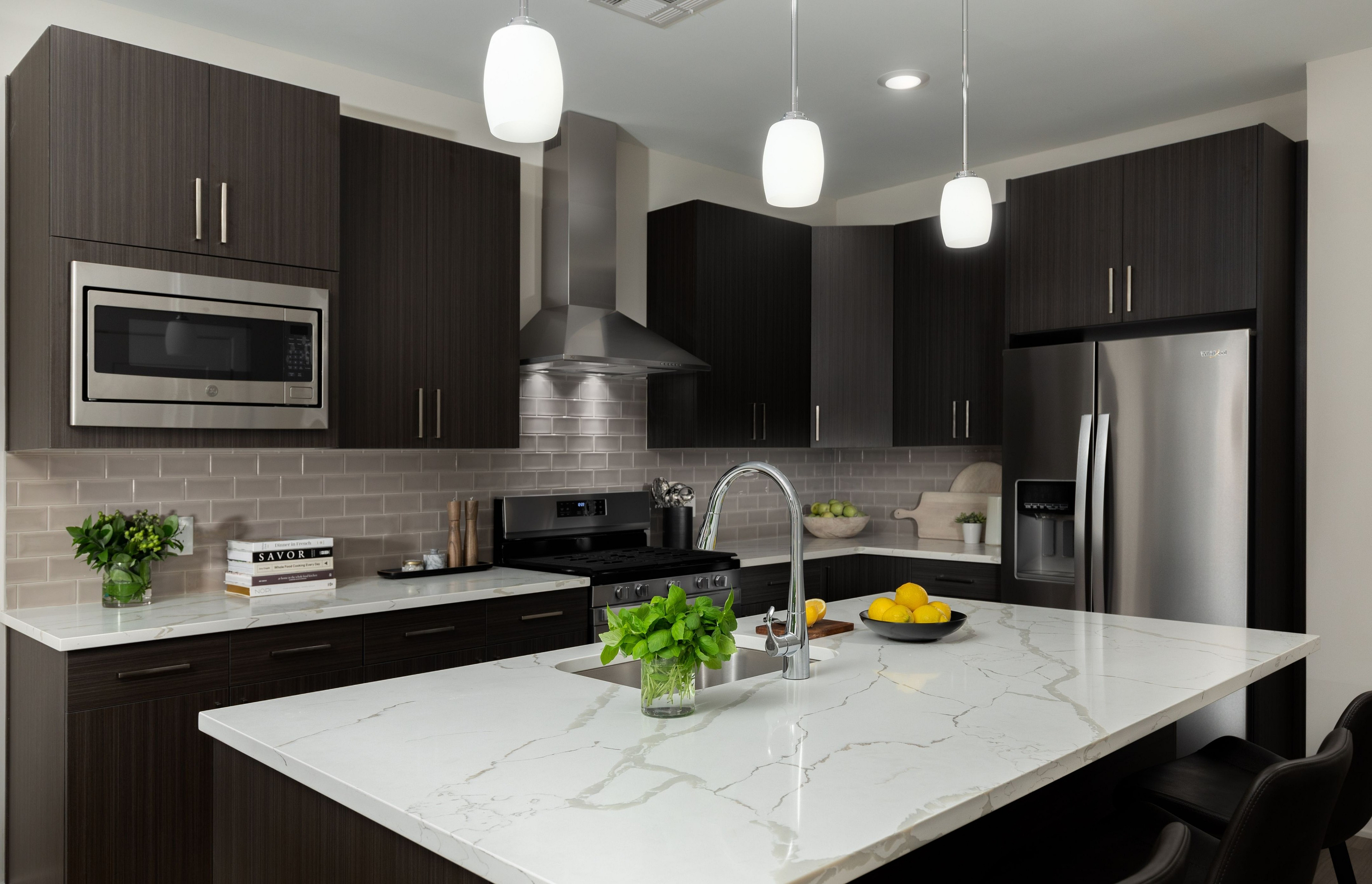 Contemporary kitchen with dark wood cabinets, stainless steel appliances, and a white marble island.