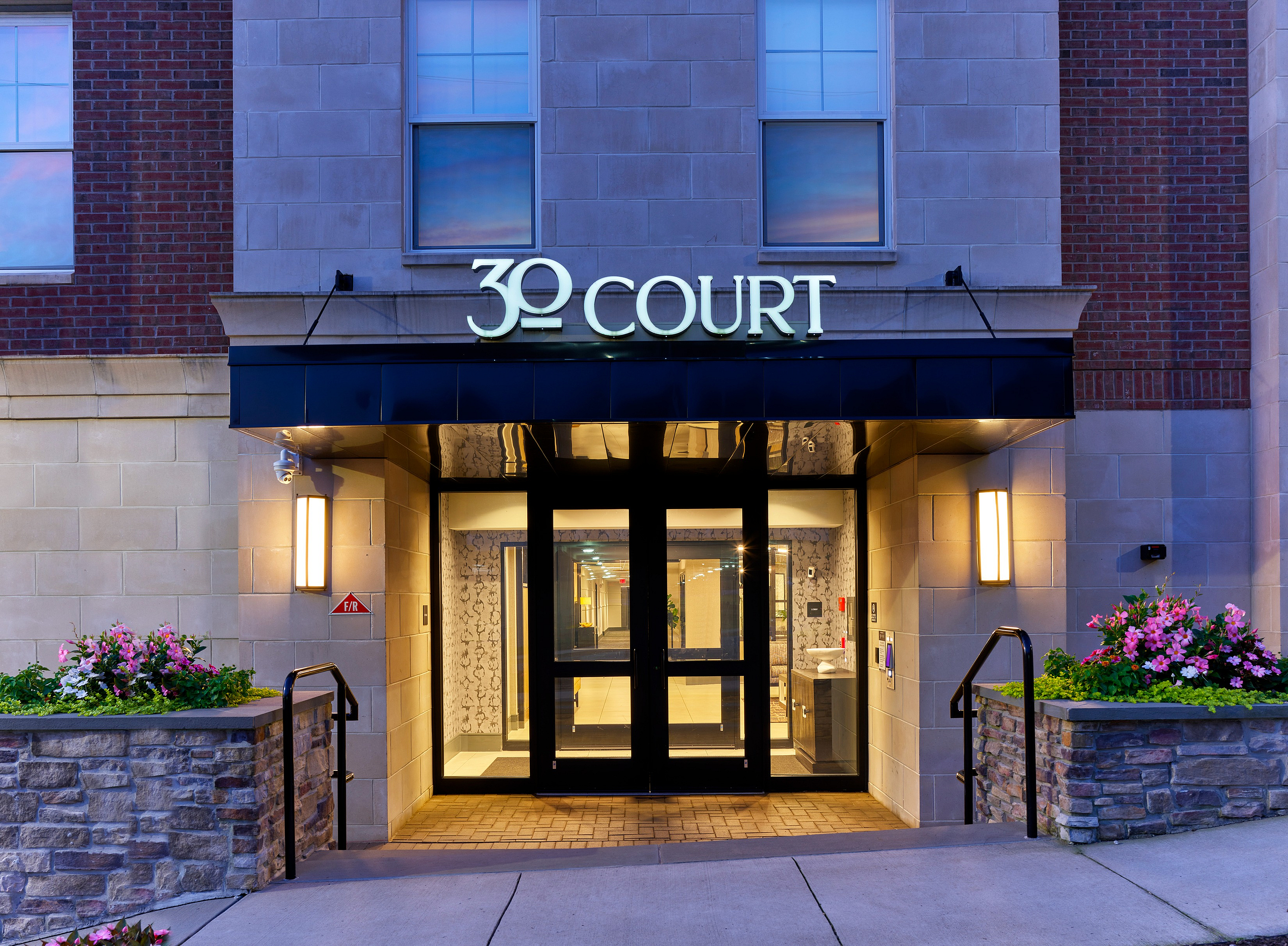 Chic entrance of a modern apartment complex with illuminated signage and floral accents.