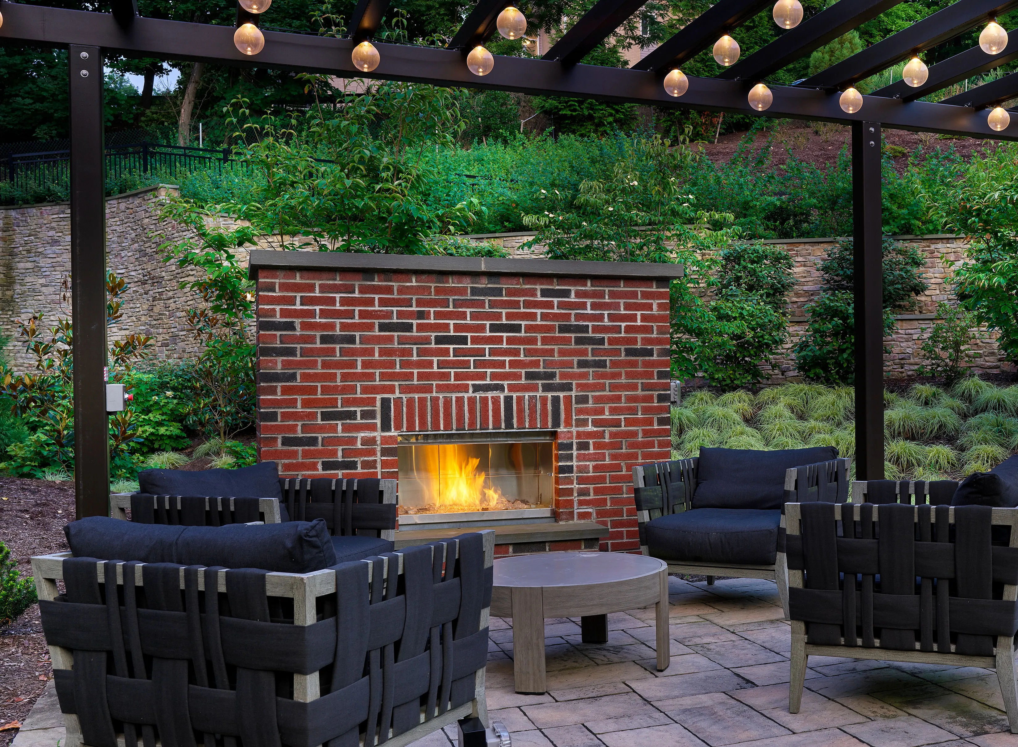 Charming outdoor patio with a modern brick fireplace, surrounded by plush seating and lush greenery.