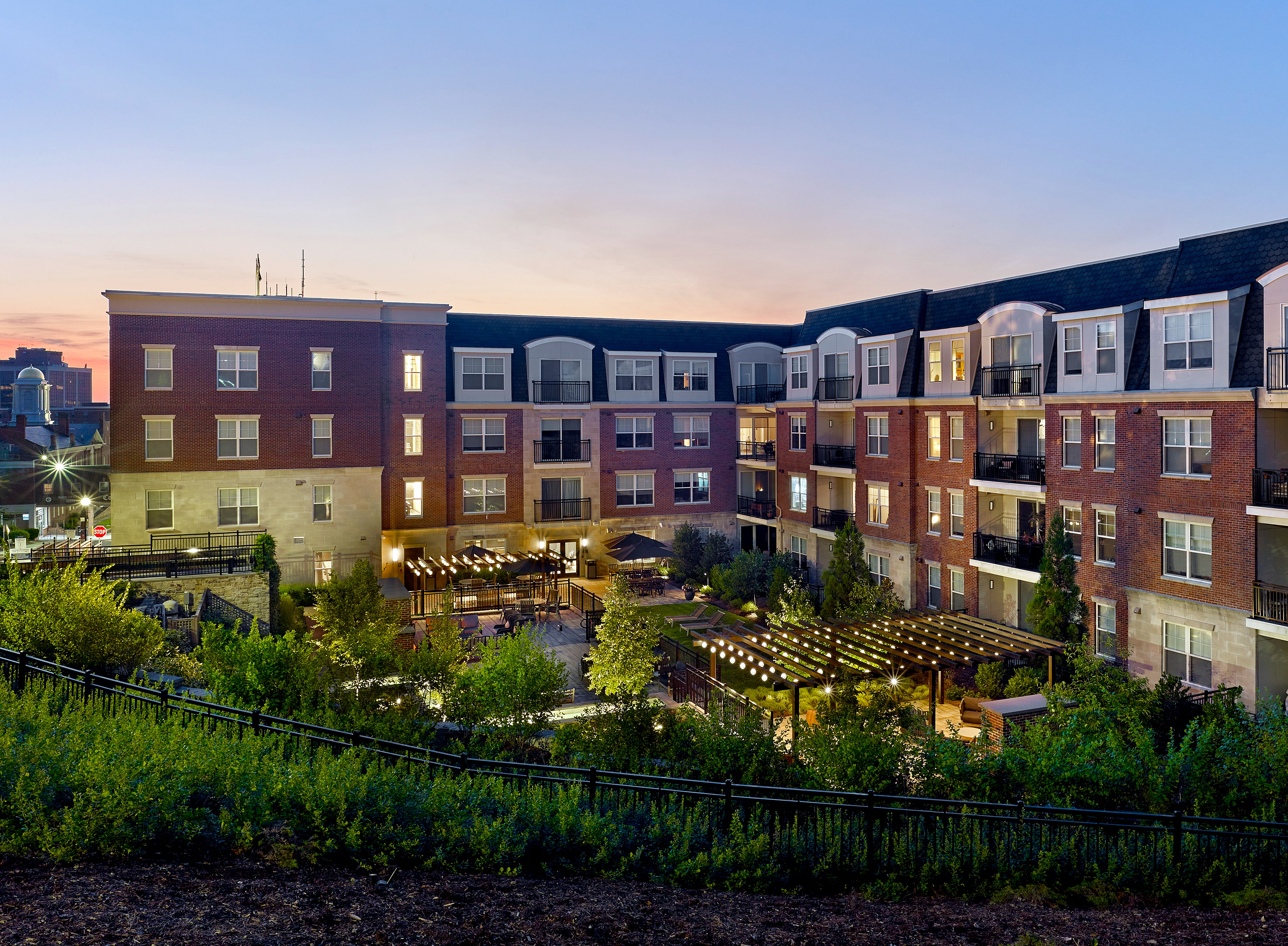 Elegant apartment complex at dusk with illuminated courtyard and lush landscaping.