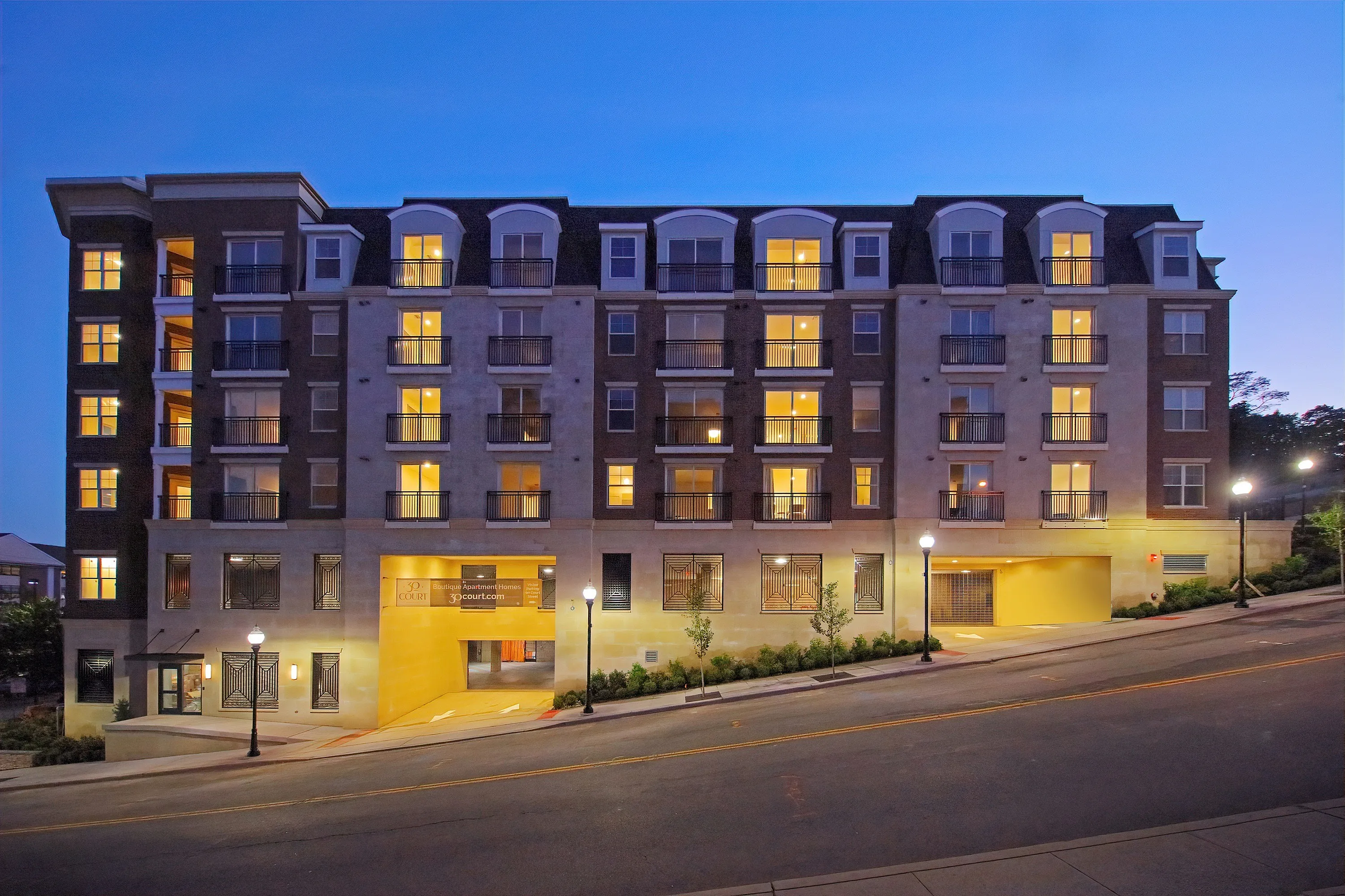 Chic multi-story apartment building with modern lighting at dusk, featuring large windows and balconies.