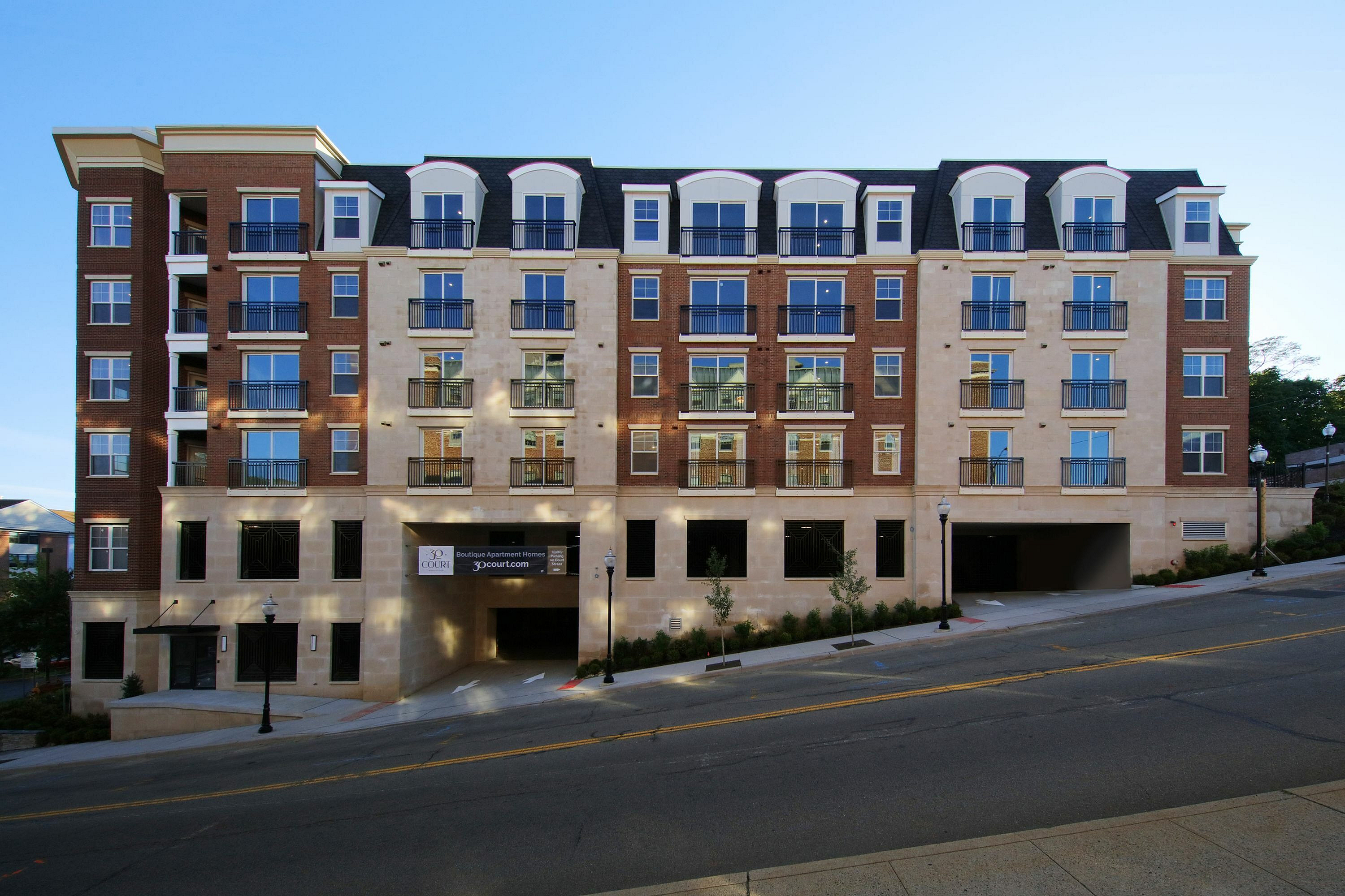 Contemporary multi-story apartment building with large windows and balconies on a sloped street.