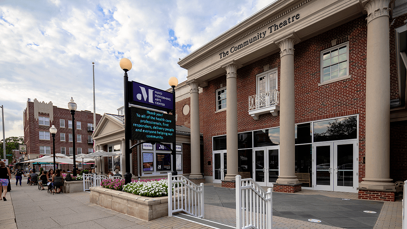Charming brick Community Theatre with classic pillars, vibrant outdoor seating area, and lively street ambiance.