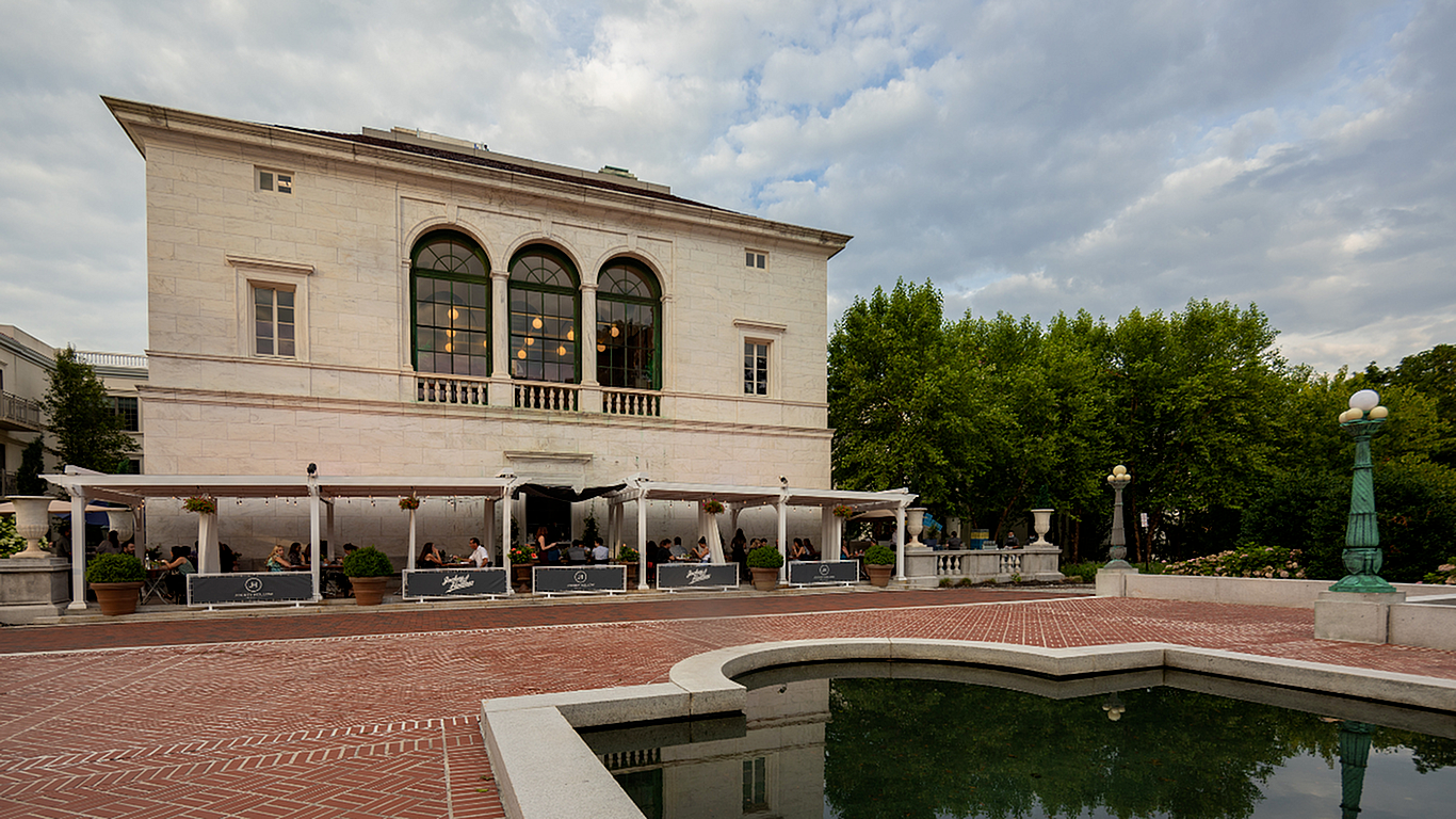 Elegant historic building with arched windows and an inviting outdoor dining area, surrounded by lush greenery and a serene water feature.
