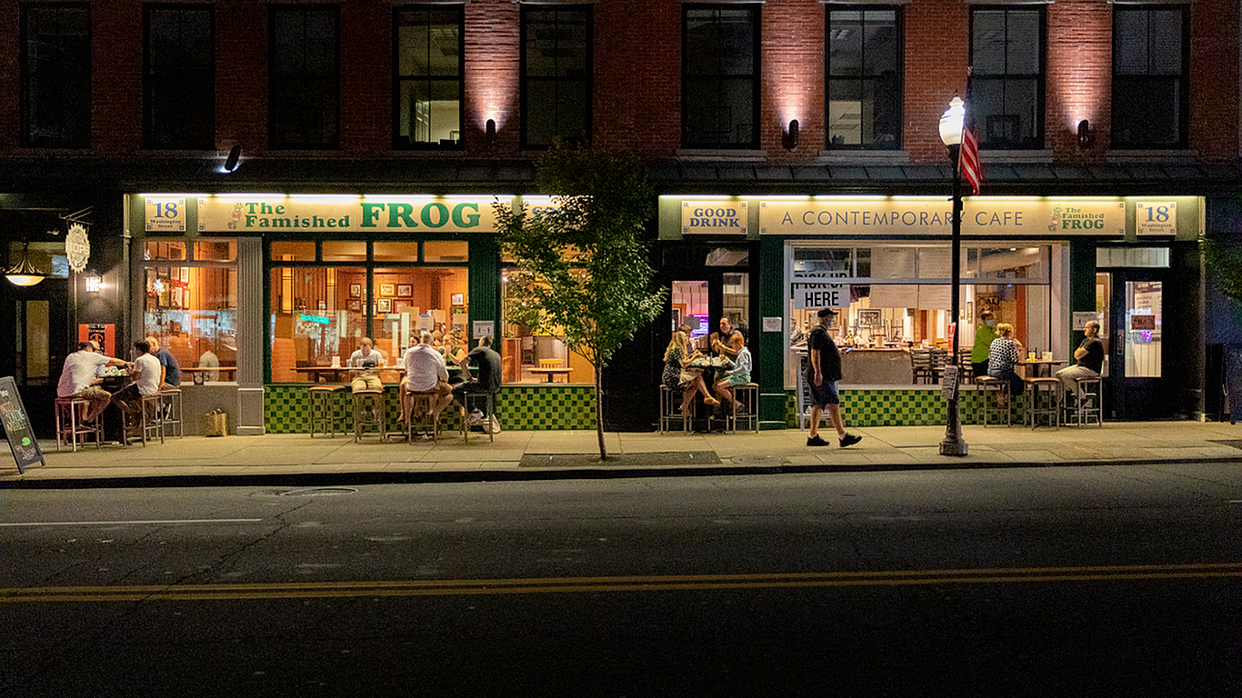 Charming evening street view featuring a lively, well-lit contemporary cafe with outdoor seating and people enjoying their time.
