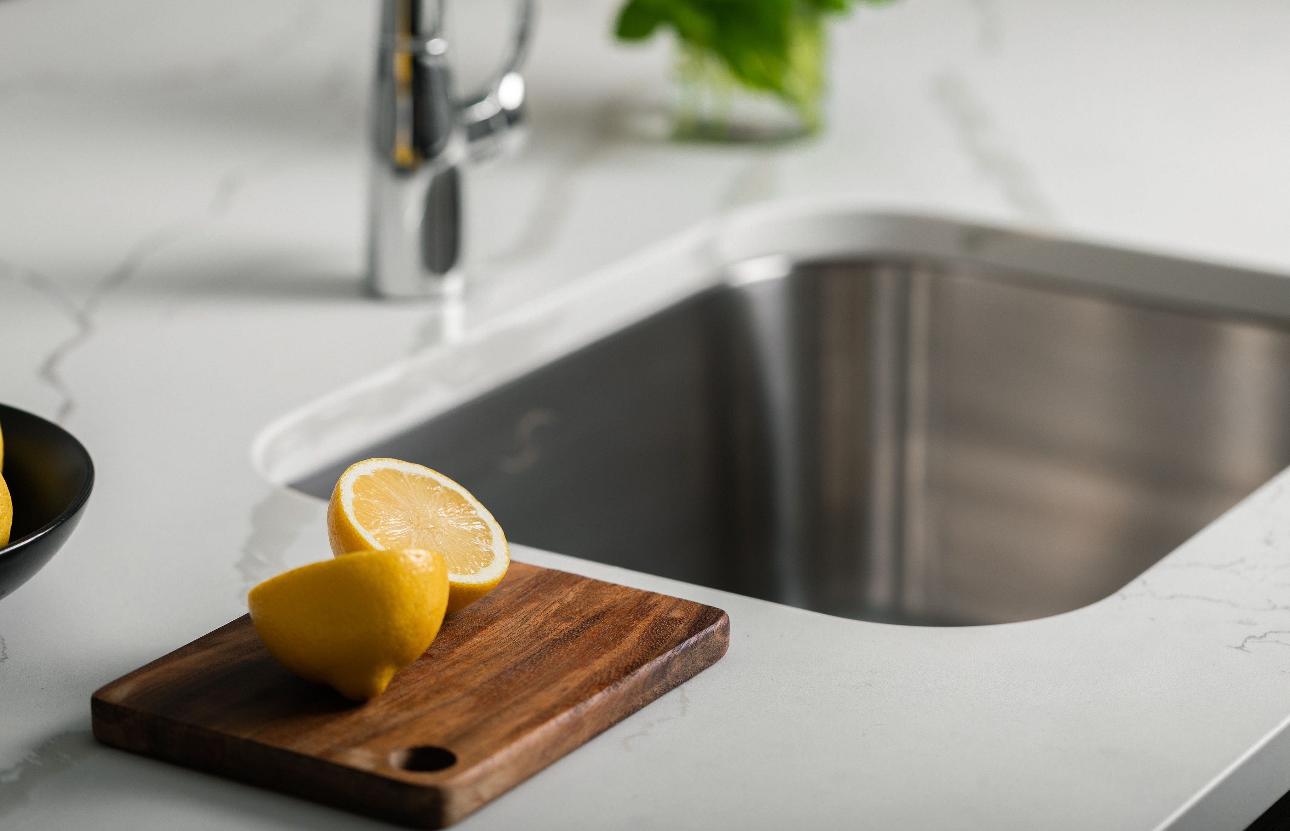 Modern kitchen sink with sleek stainless-steel design, complemented by a fresh cut lemon on a wooden board, showcasing a stylish and functional space.