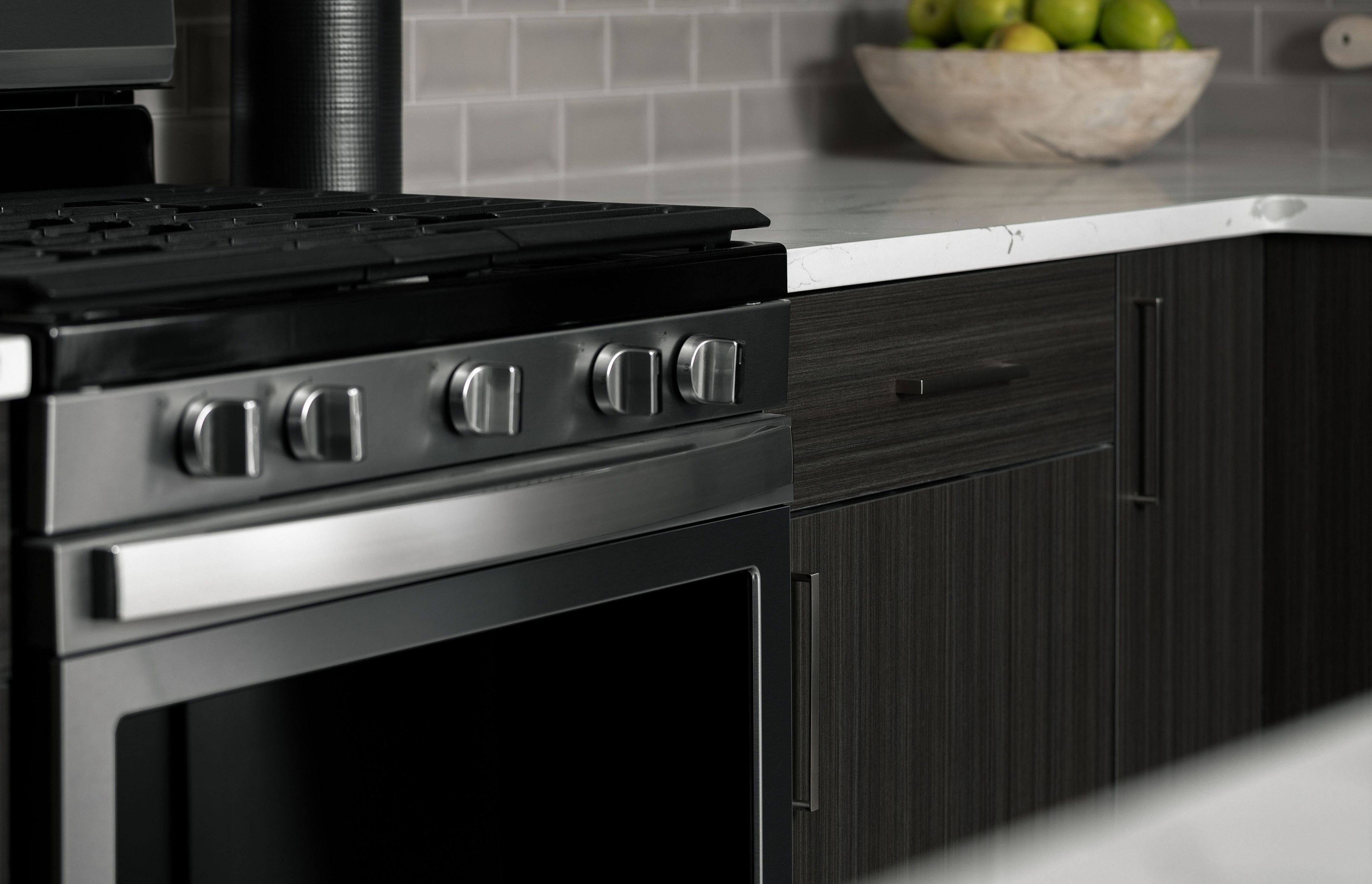 Elegant kitchen with sleek stainless steel oven, modern cabinetry, and chic countertop adorned with a bowl of fresh green apples.