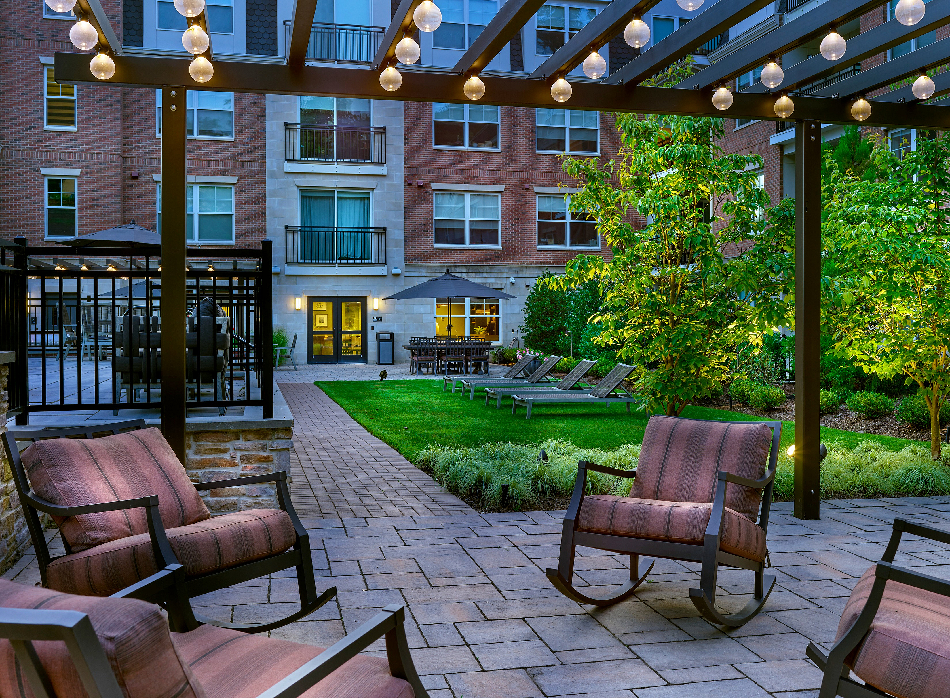 Charming outdoor courtyard with modern seating, lush greenery, and ambient lighting, perfect for relaxation.
