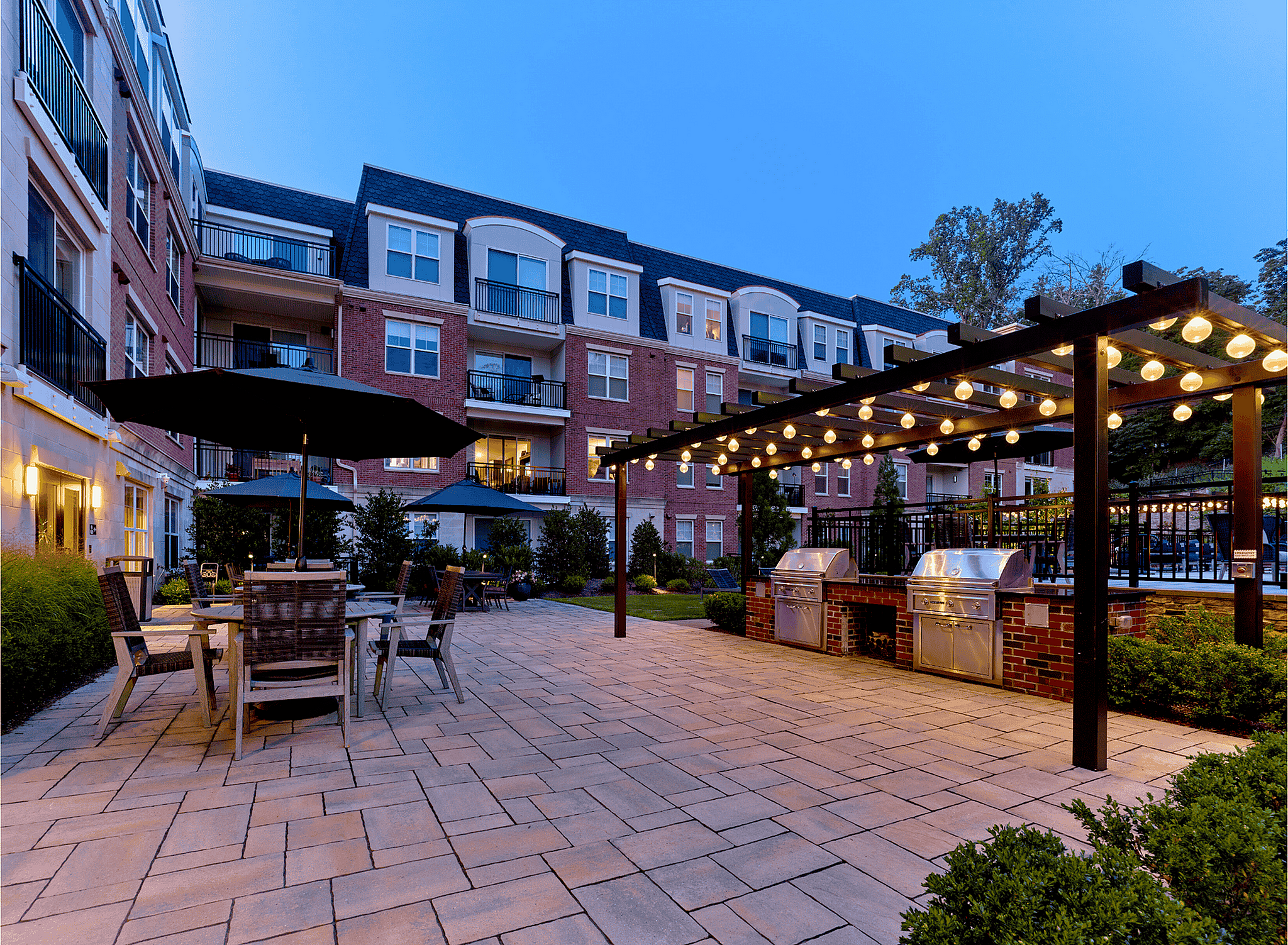 Charming outdoor communal space with cozy seating, elegant lighting, and modern grills, set against a stylish apartment building backdrop.