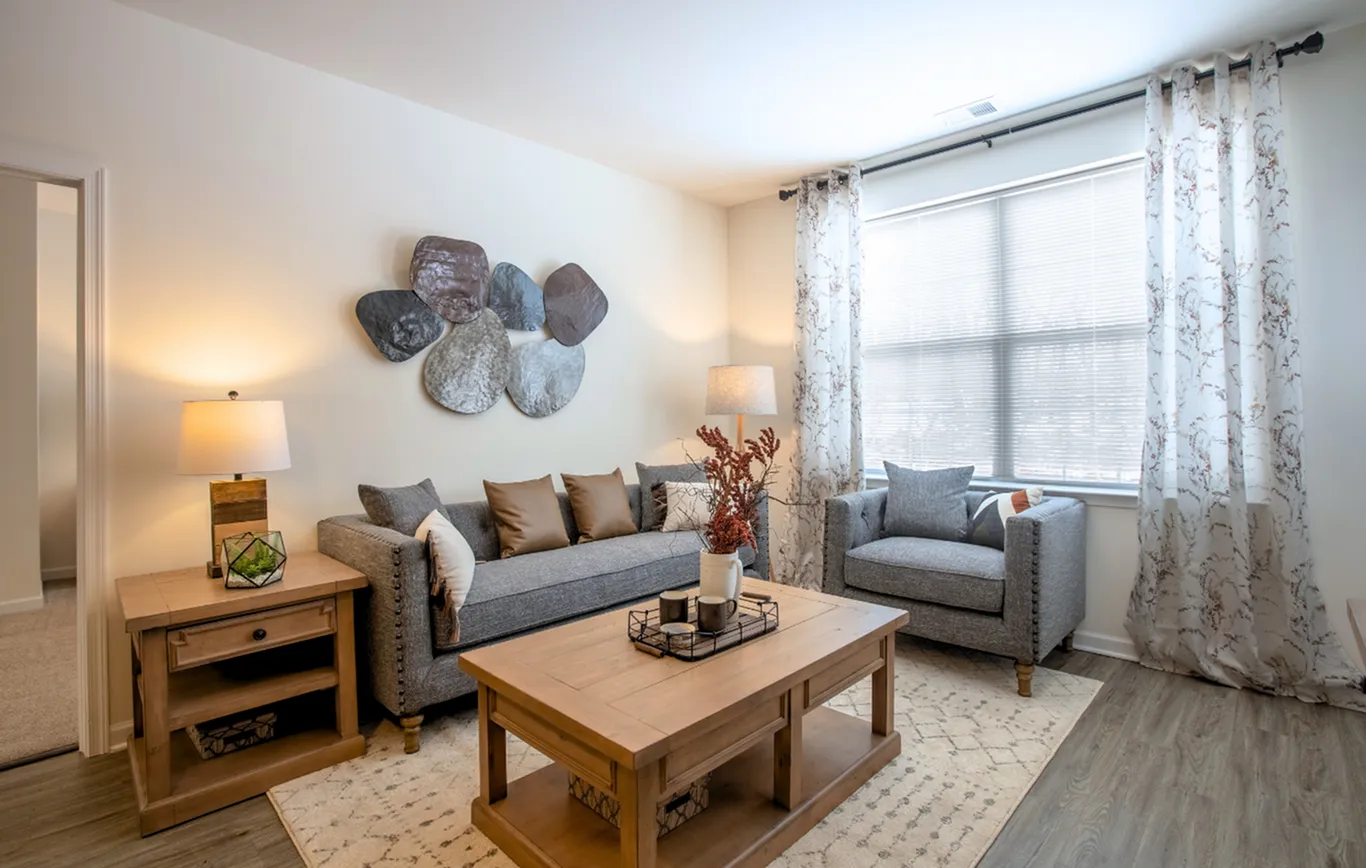 Bright and inviting living room with modern decor, showcasing a cozy gray sofa and armchair, wooden coffee table, and elegant wall art.
