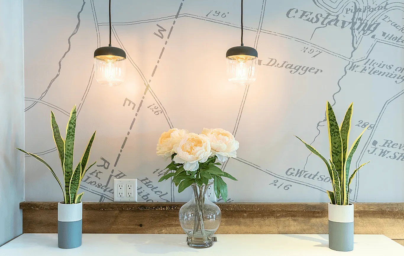 Chic and modern interior with elegant pendant lights, vibrant snake plants, and a bouquet of soft white flowers in a glass vase against a stylish map-themed wall.