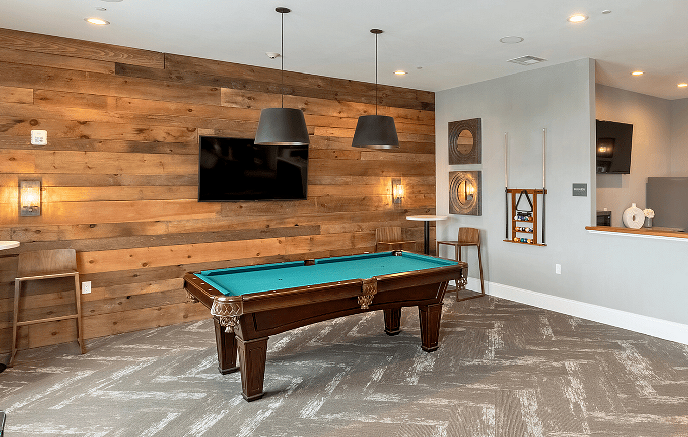 Chic recreation room with a pool table, rustic wood paneling, modern lighting, and stylish decor.