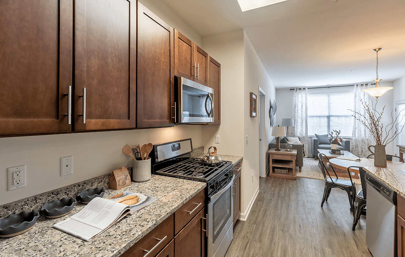 Inviting modern kitchen with elegant wooden cabinets and granite countertops leads into a cozy living space with natural light.