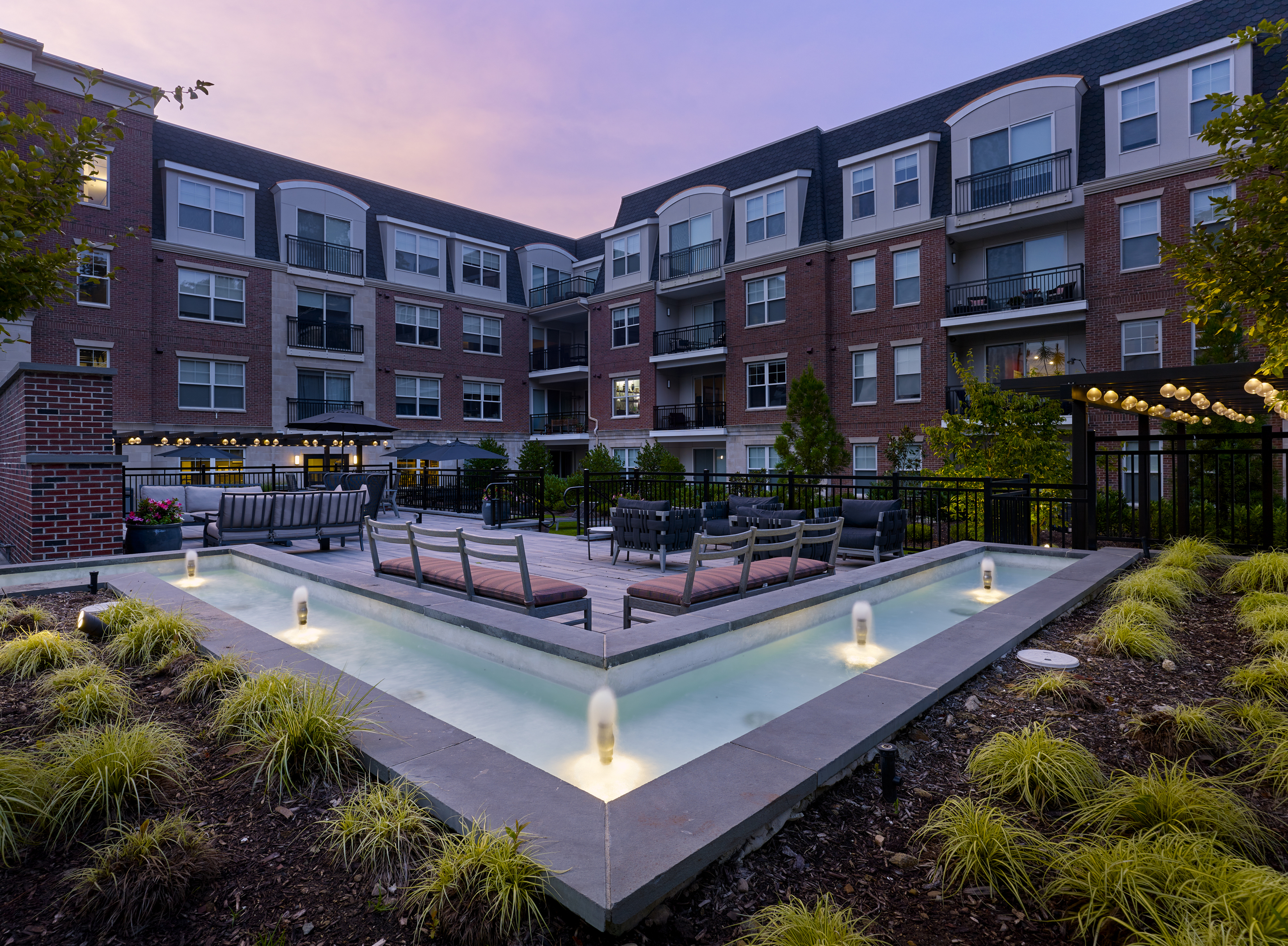 Charming apartment complex courtyard at sunset, featuring modern outdoor seating, sparkling water fountains, and lush landscaping.