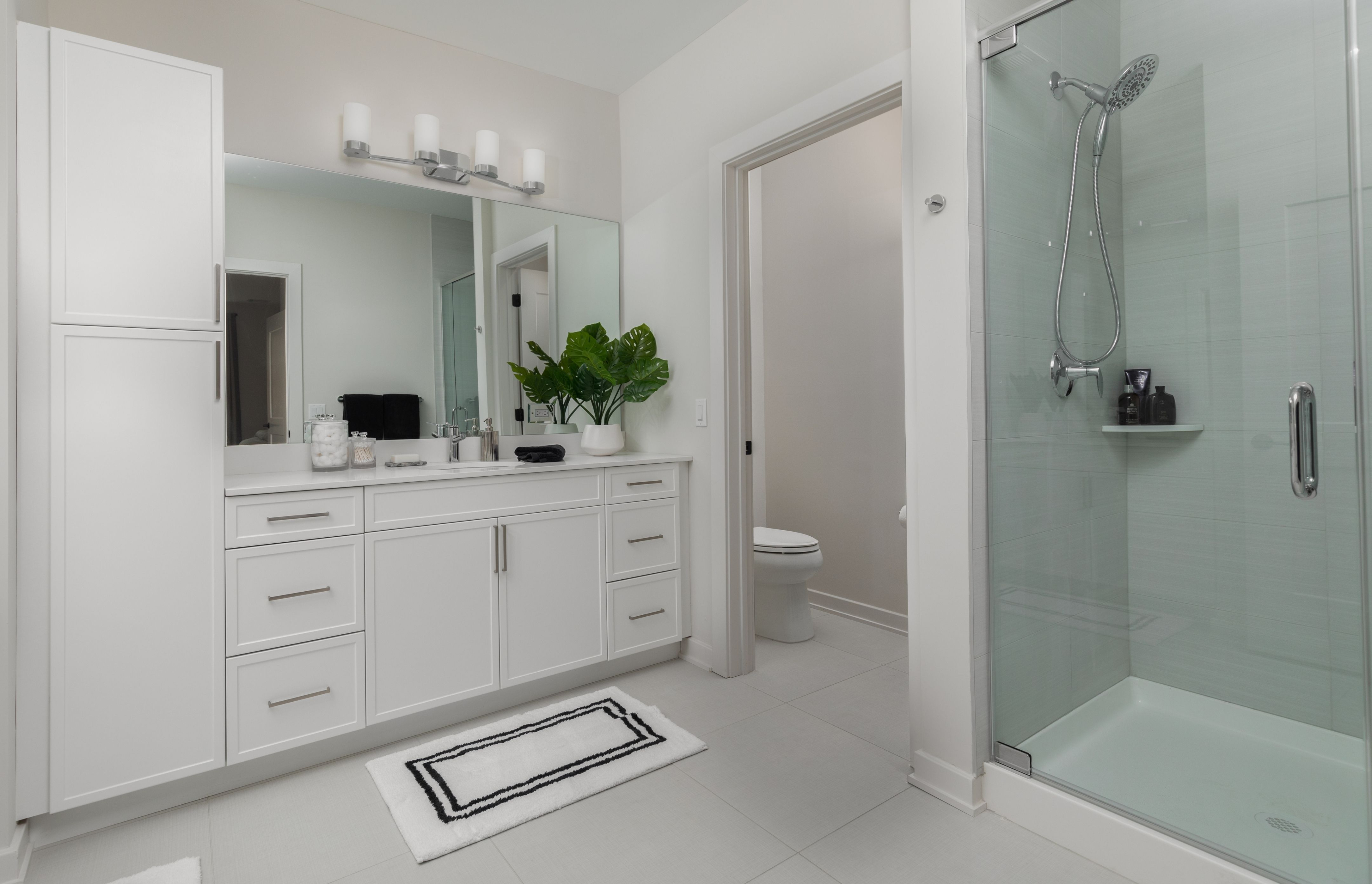 Elegant bathroom featuring a sleek glass shower, modern vanity with ample storage, and lush green decor.