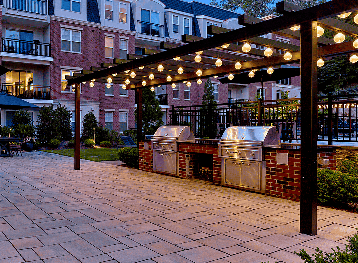 Charming apartment courtyard with illuminated pergola, outdoor seating, and modern brick grills.